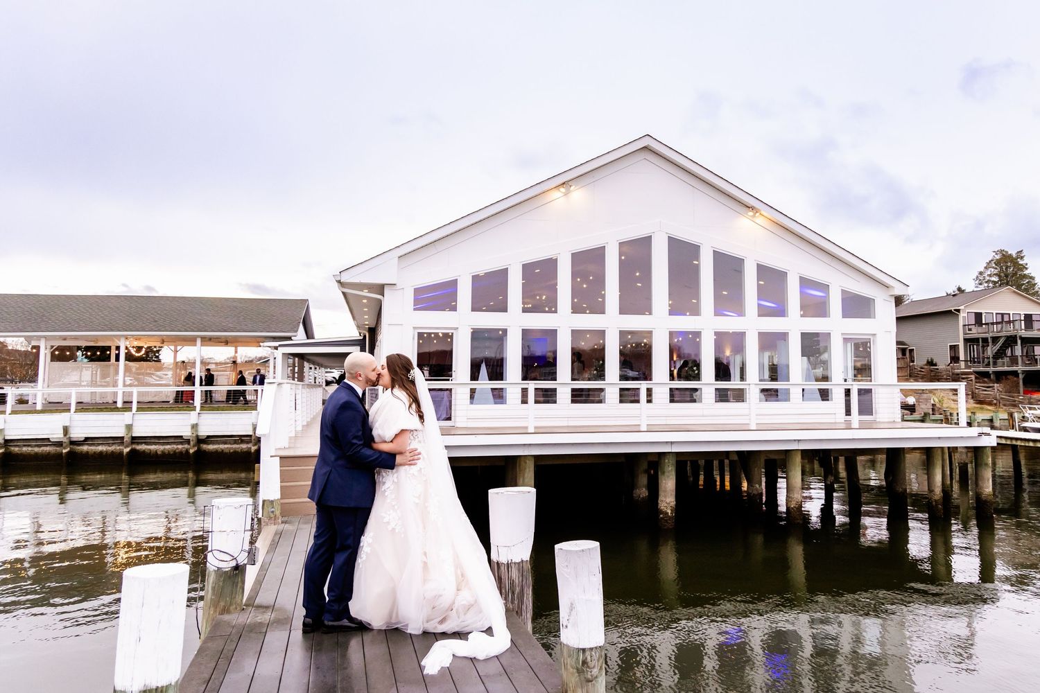 Wedding couple and guests gather on a white waterfront dock venue for a scenic celebration by the bay.
