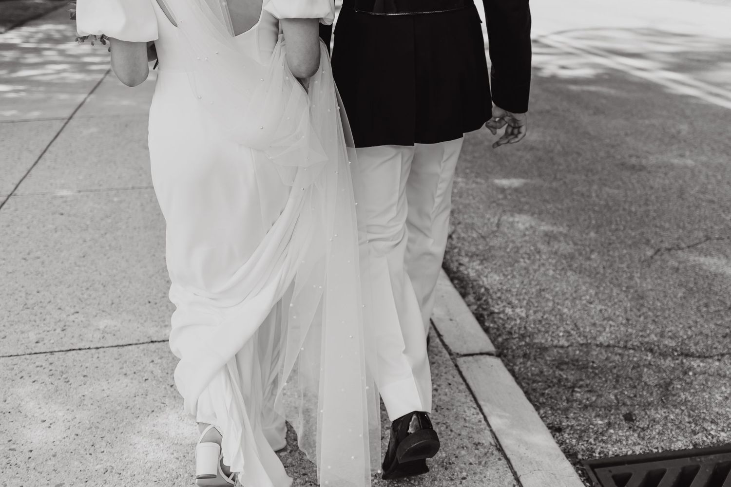A wedding couple walking together in formal attire on a sunny day.