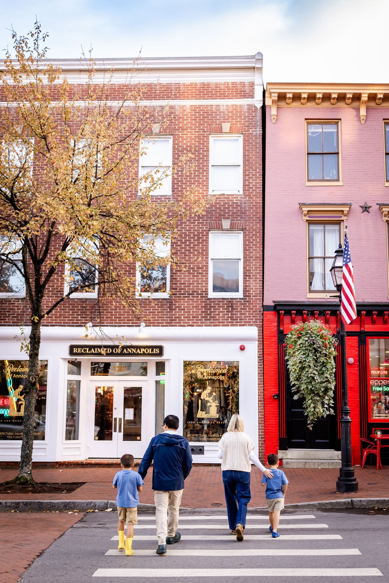 People walking along a charming brick-lined street with historic storefronts and American flags.
