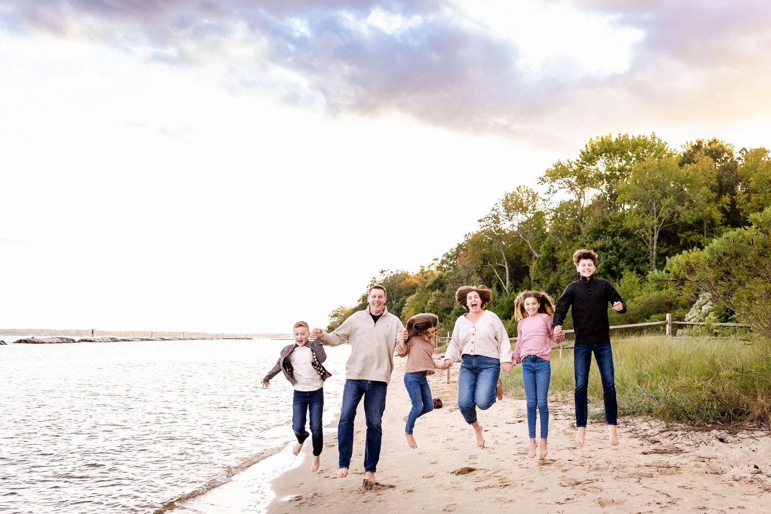 Group walking along scenic beach shoreline at sunset with trees in background.