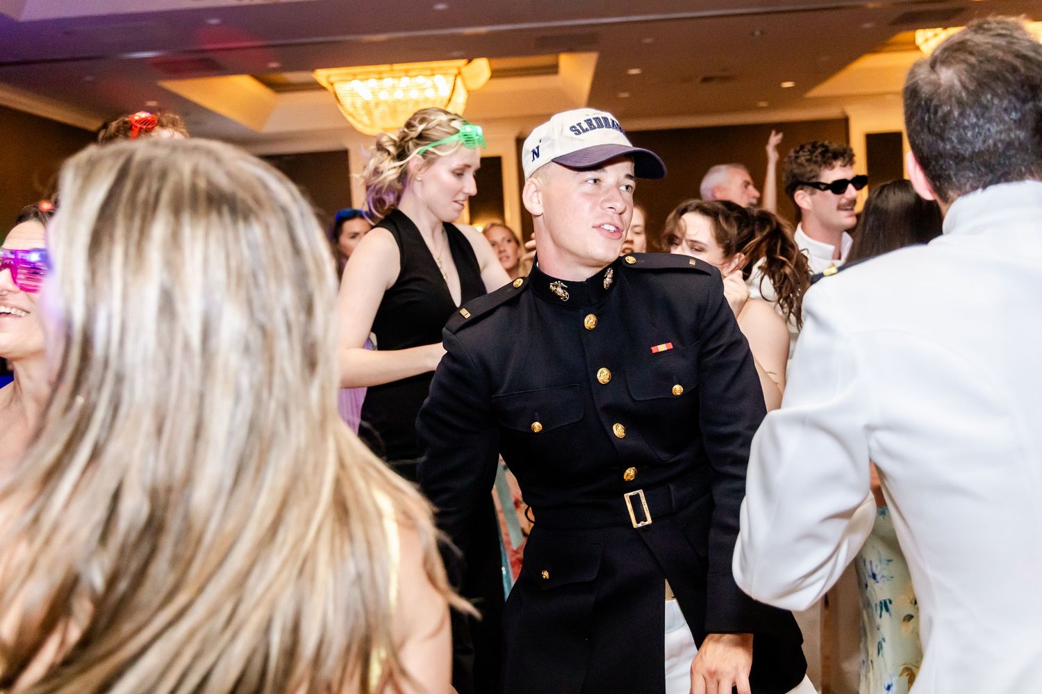 Festive wedding party dancing and celebrating during reception under warm ballroom lighting.