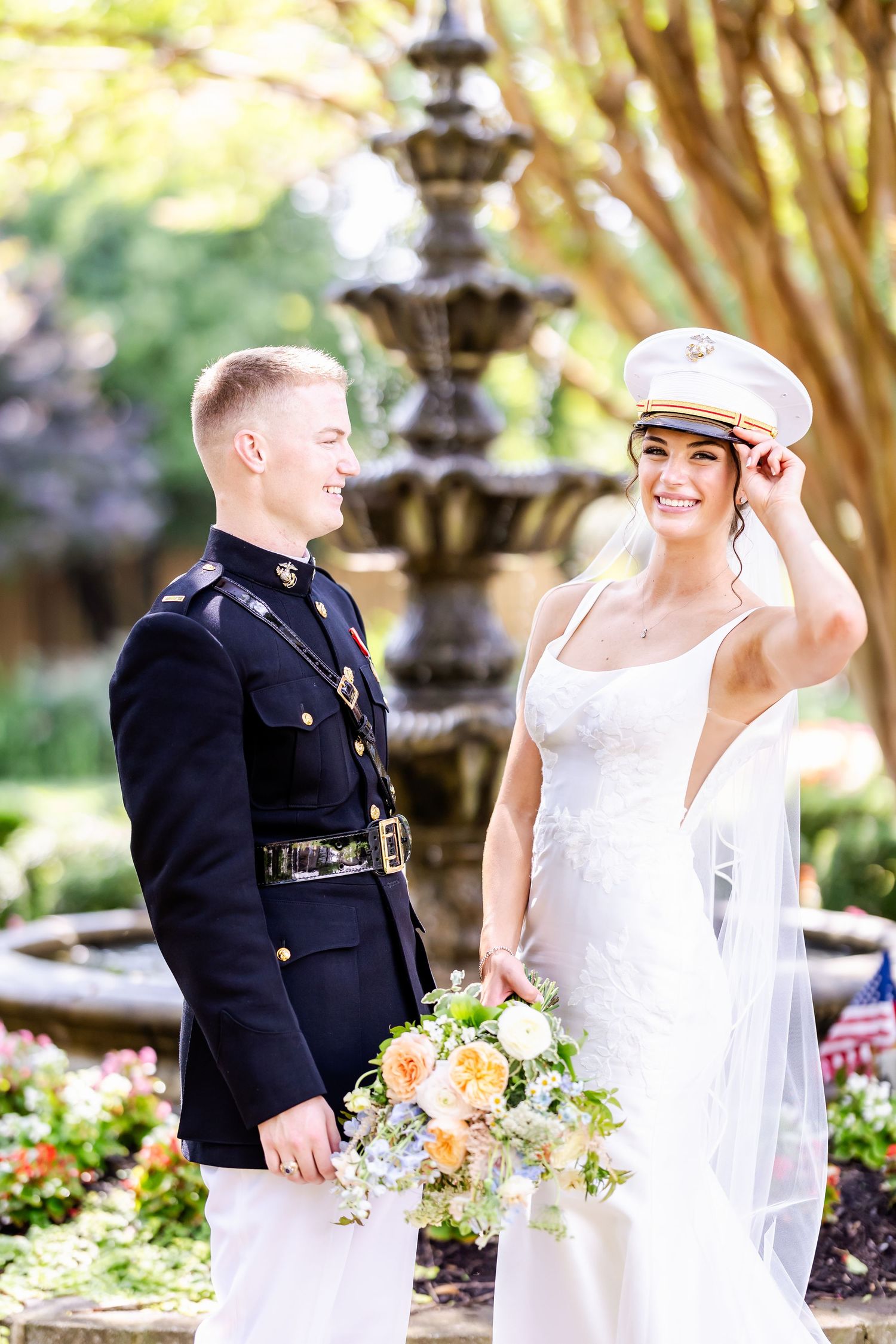 Military groom and bride in white dress pose together in a garden setting with flowers and lanterns.