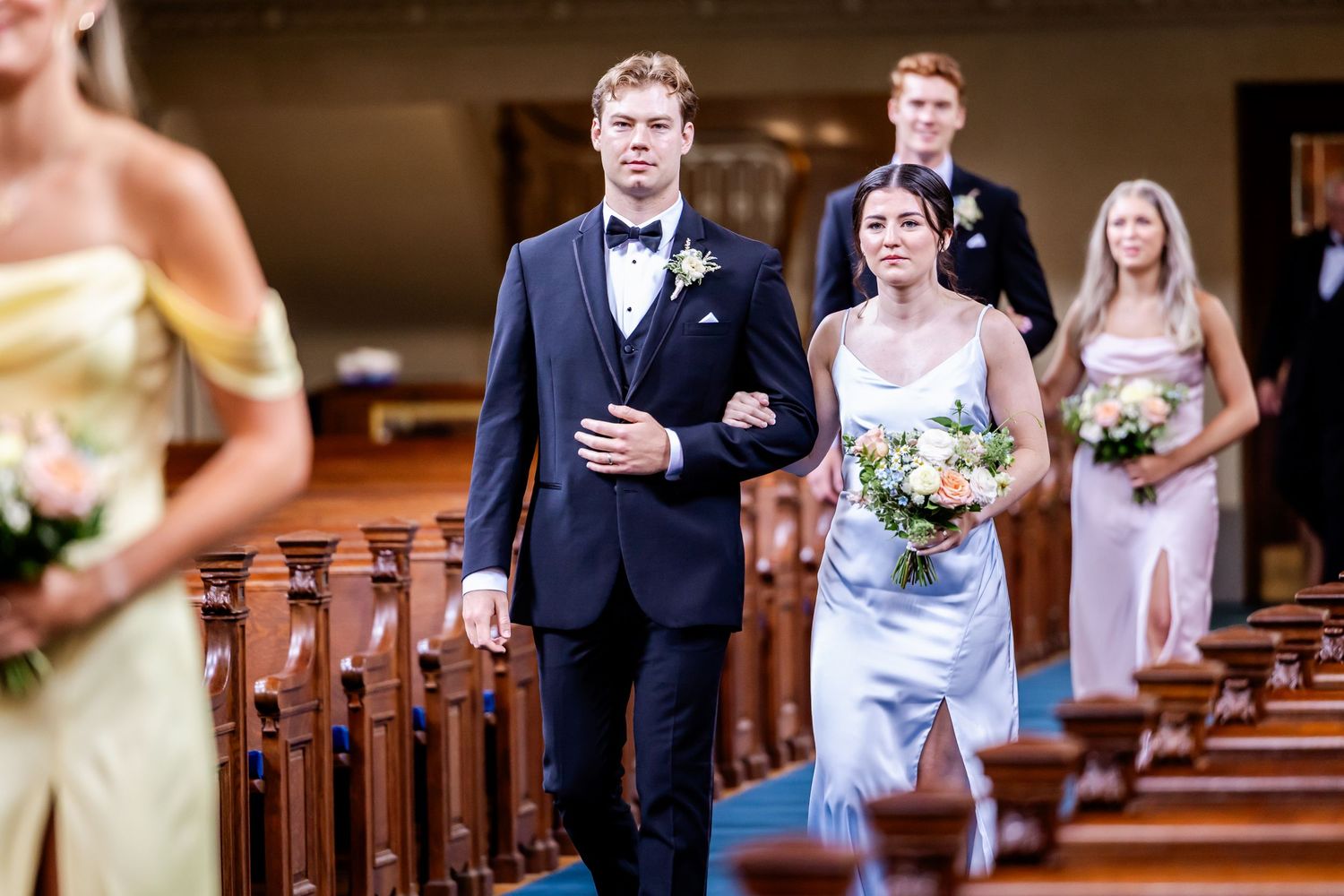 Wedding party members walking down the aisle in a traditional church ceremony.