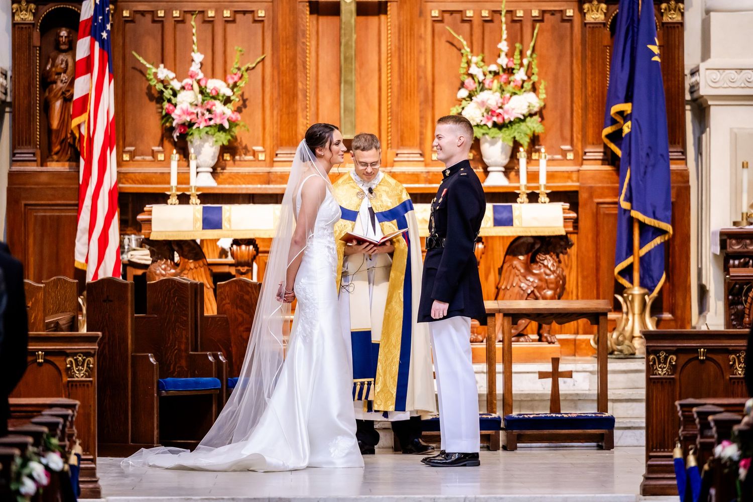 Military wedding ceremony in a traditional church with American flags and floral arrangements.
