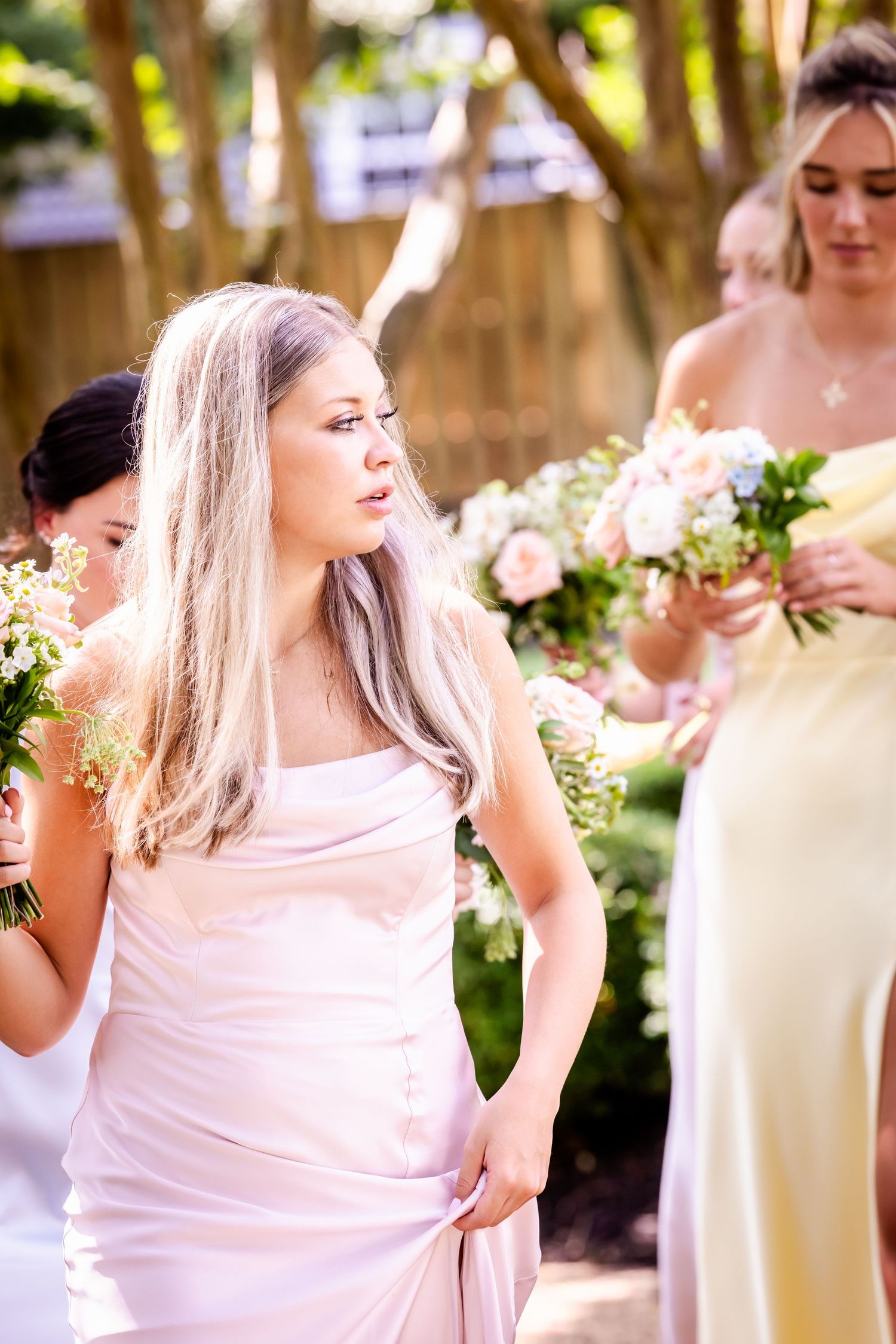 Bridesmaids in light colored dresses pose together outdoors in natural lighting.
