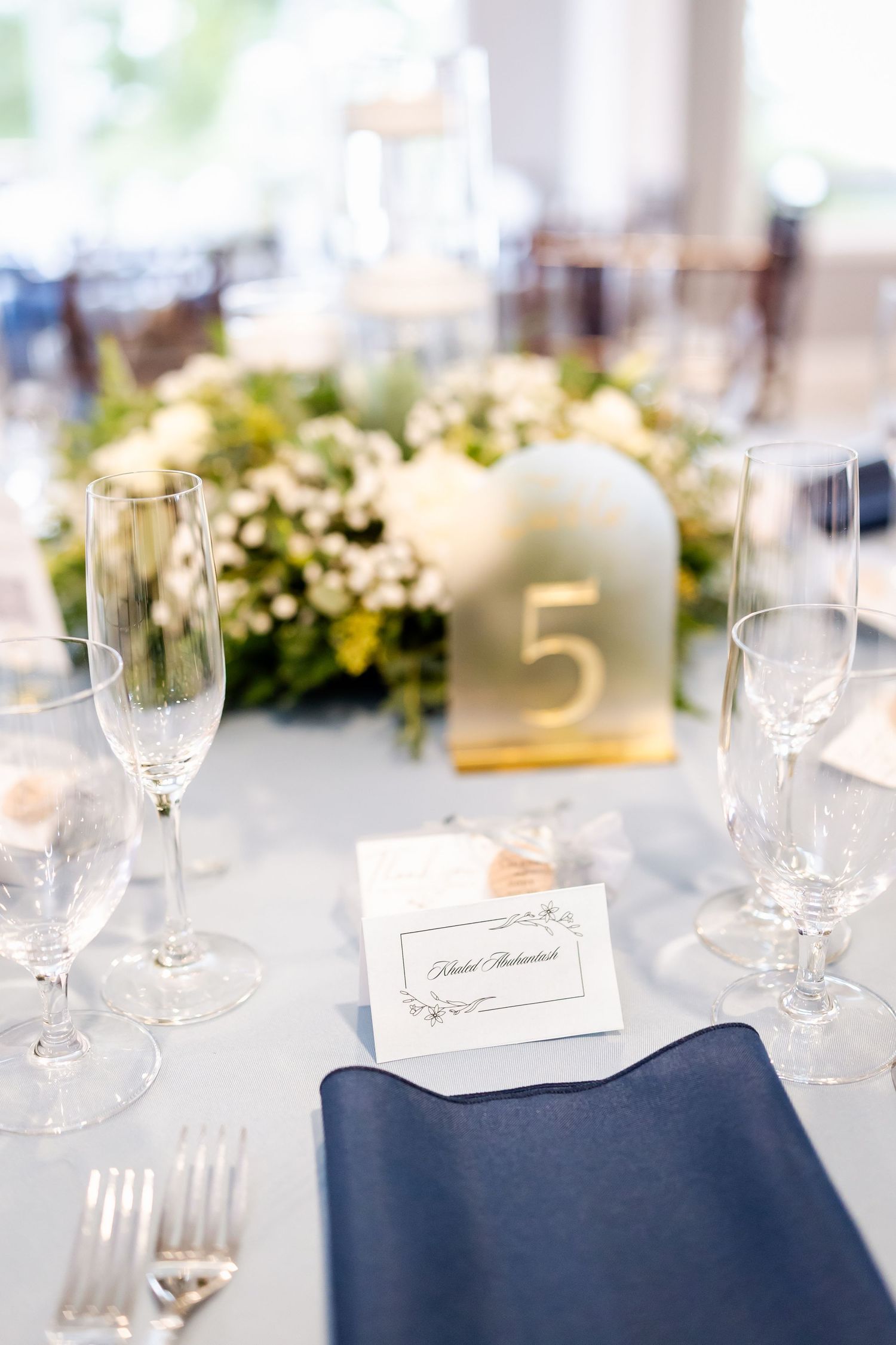 Elegant wedding reception table setting with navy blue napkins and crystal glassware.