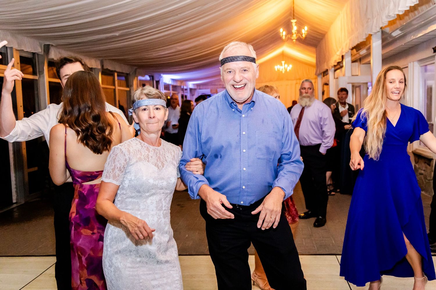 Guests enjoying dance floor festivities at wedding reception with warm lighting and fabric decor.