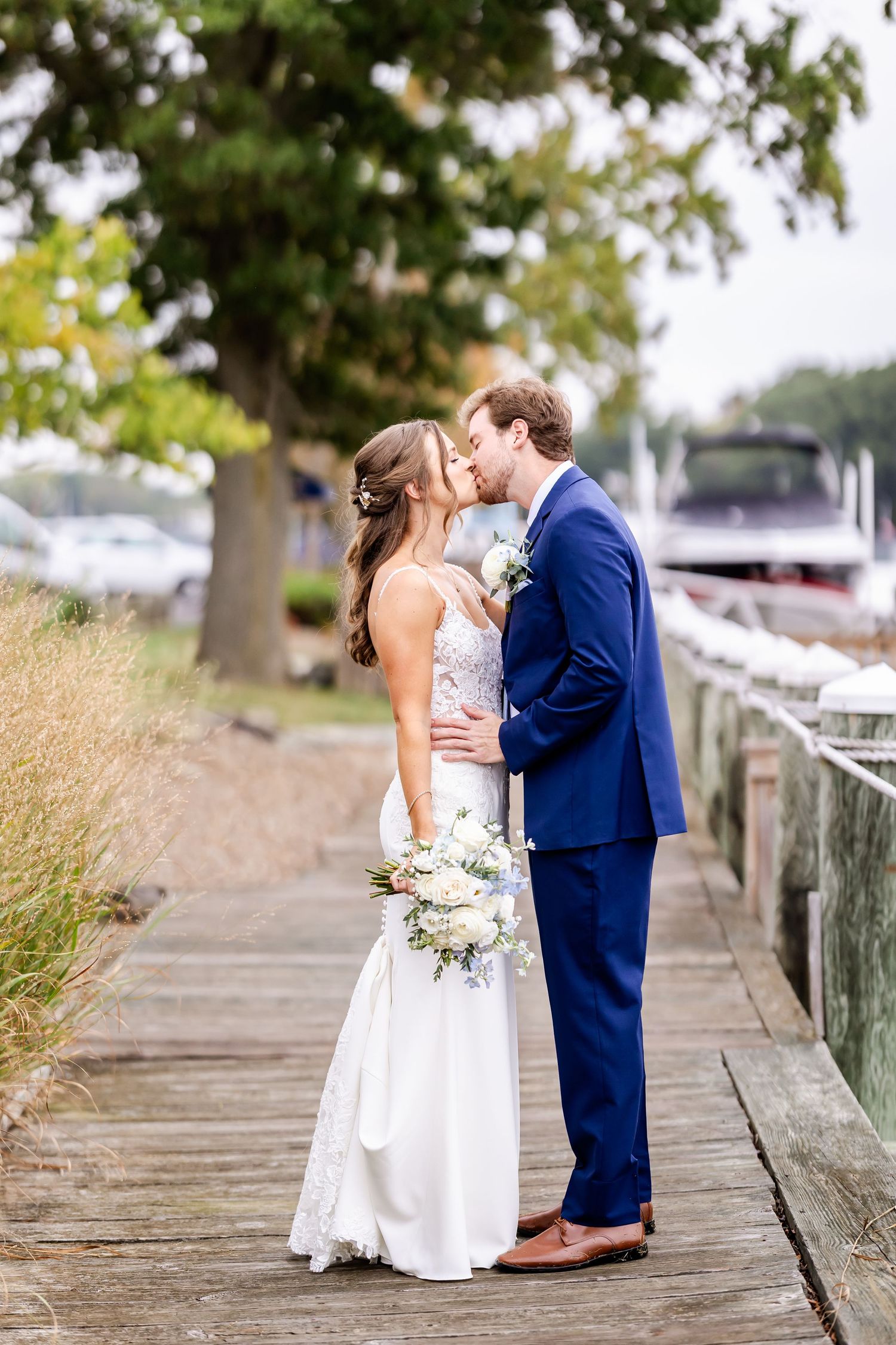 A romantic wedding couple shares intimate moments on a wooden boardwalk by the water.