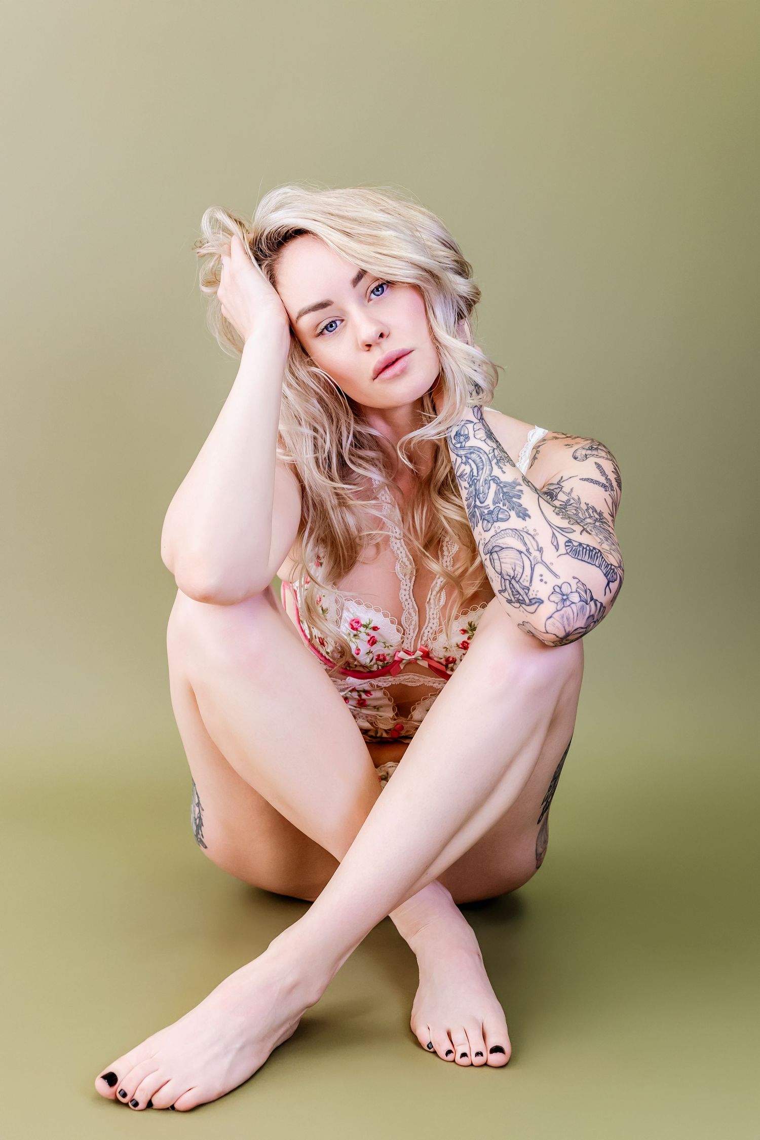 Close-up artistic photo showing bare feet and tattooed arm against a neutral green background.