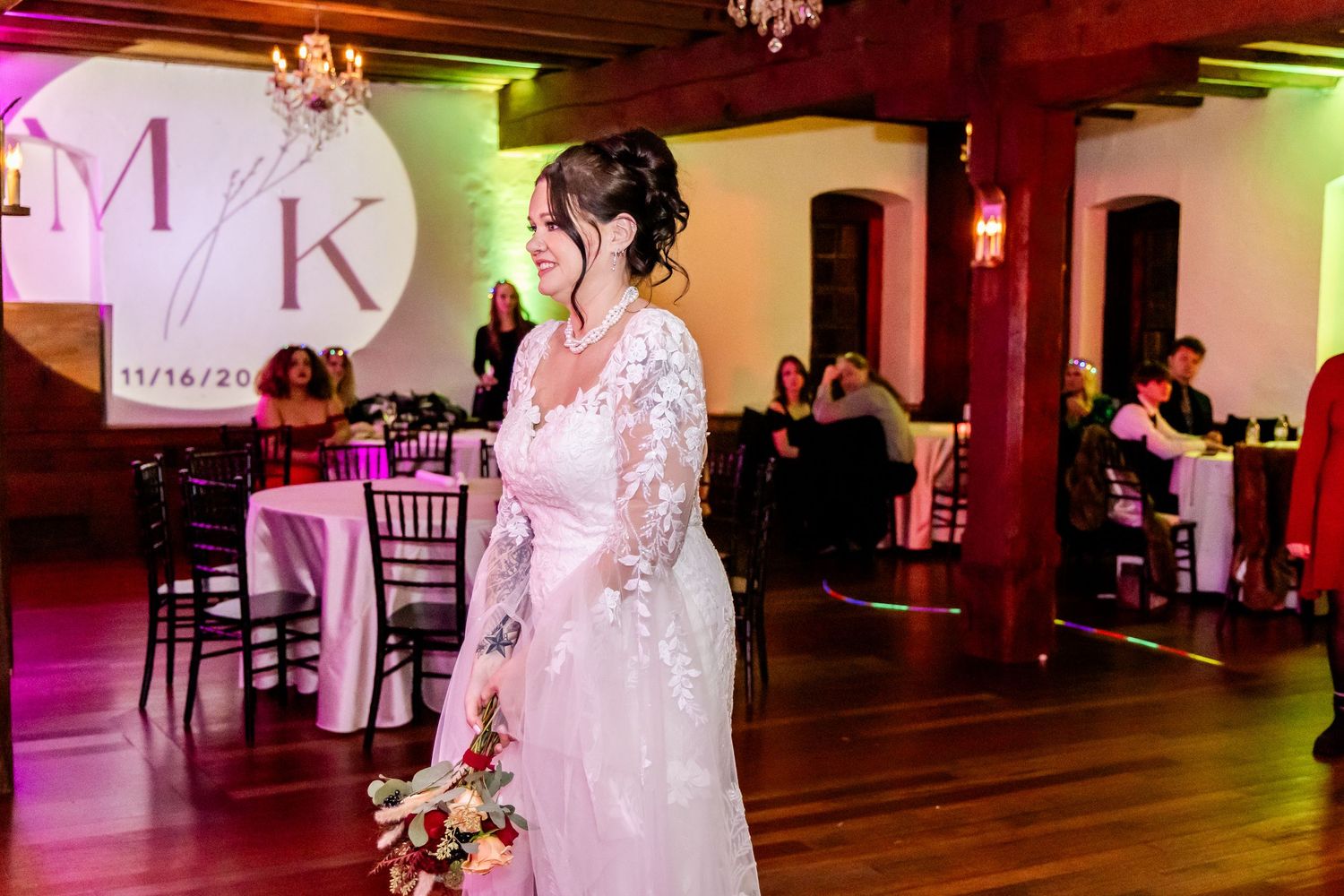 A wedding celebration in an elegant venue with exposed beams and colorful mood lighting.