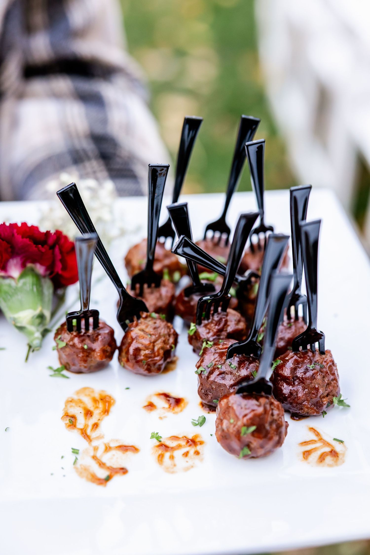 Elegant appetizer meatballs with decorative black picks served on a white tablecloth.