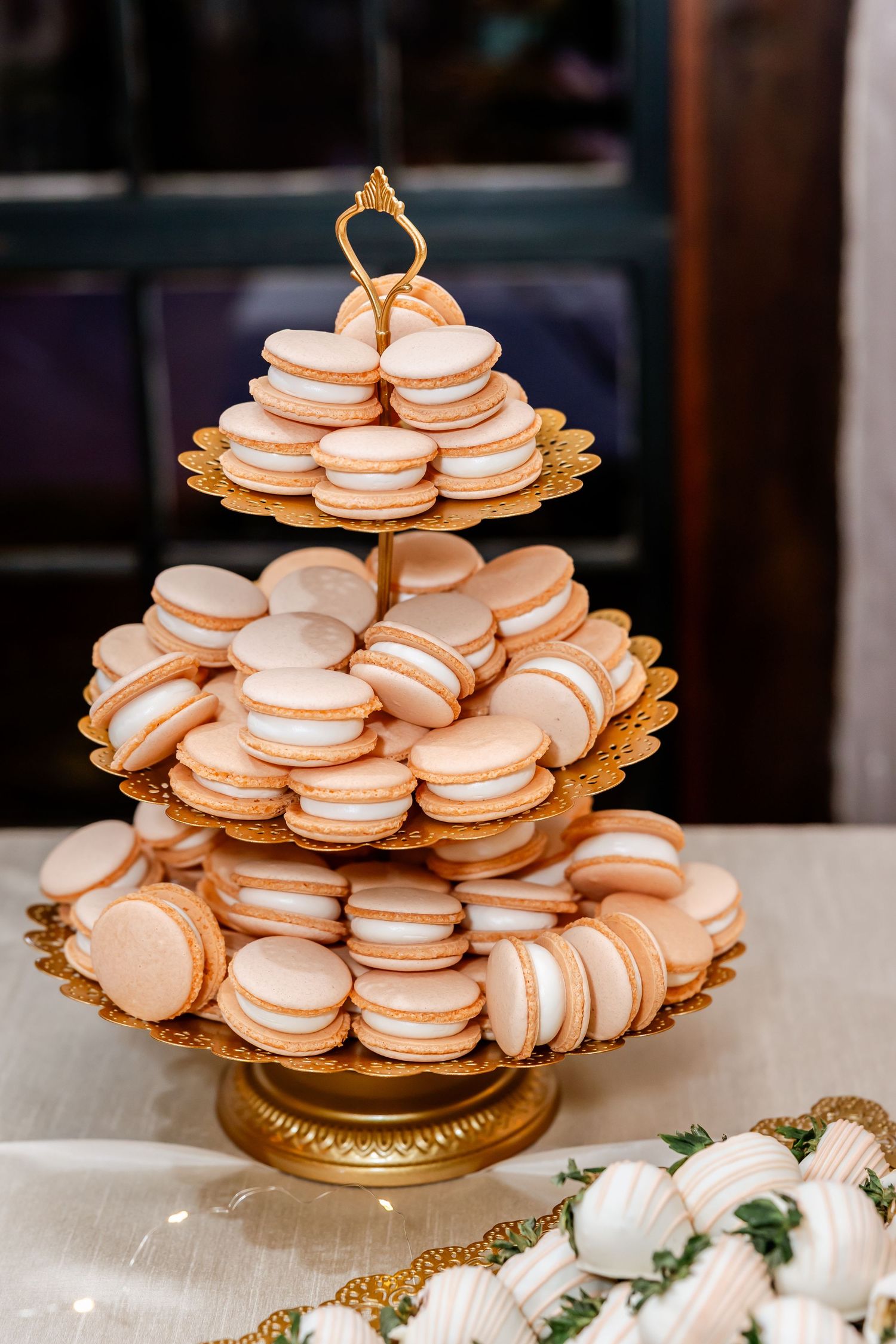 A tiered display of light pink macarons on a gold stand at a wedding dessert table.
