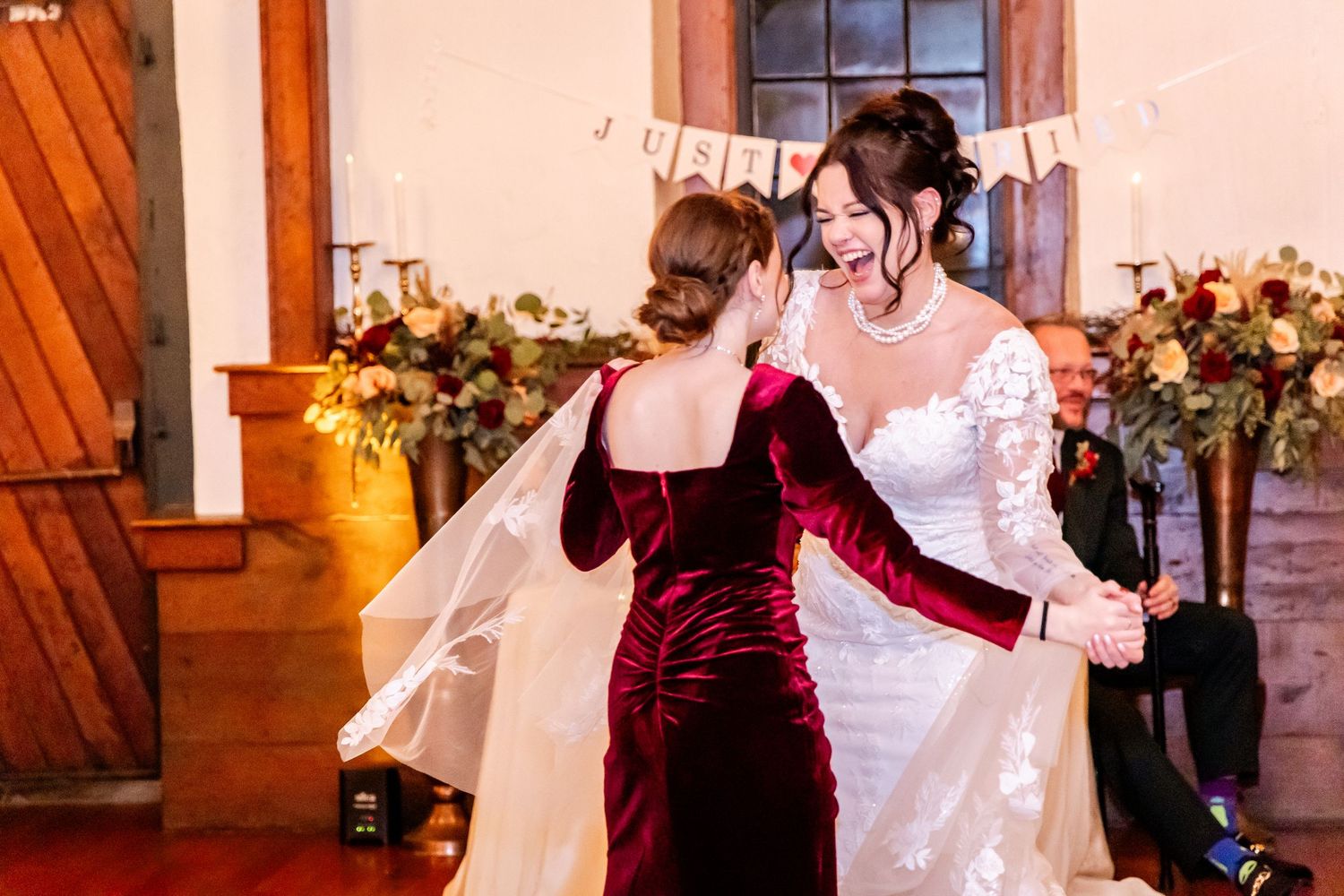 Wedding guests dancing and celebrating together on a wooden dance floor under warm lighting at an indoor reception venue.