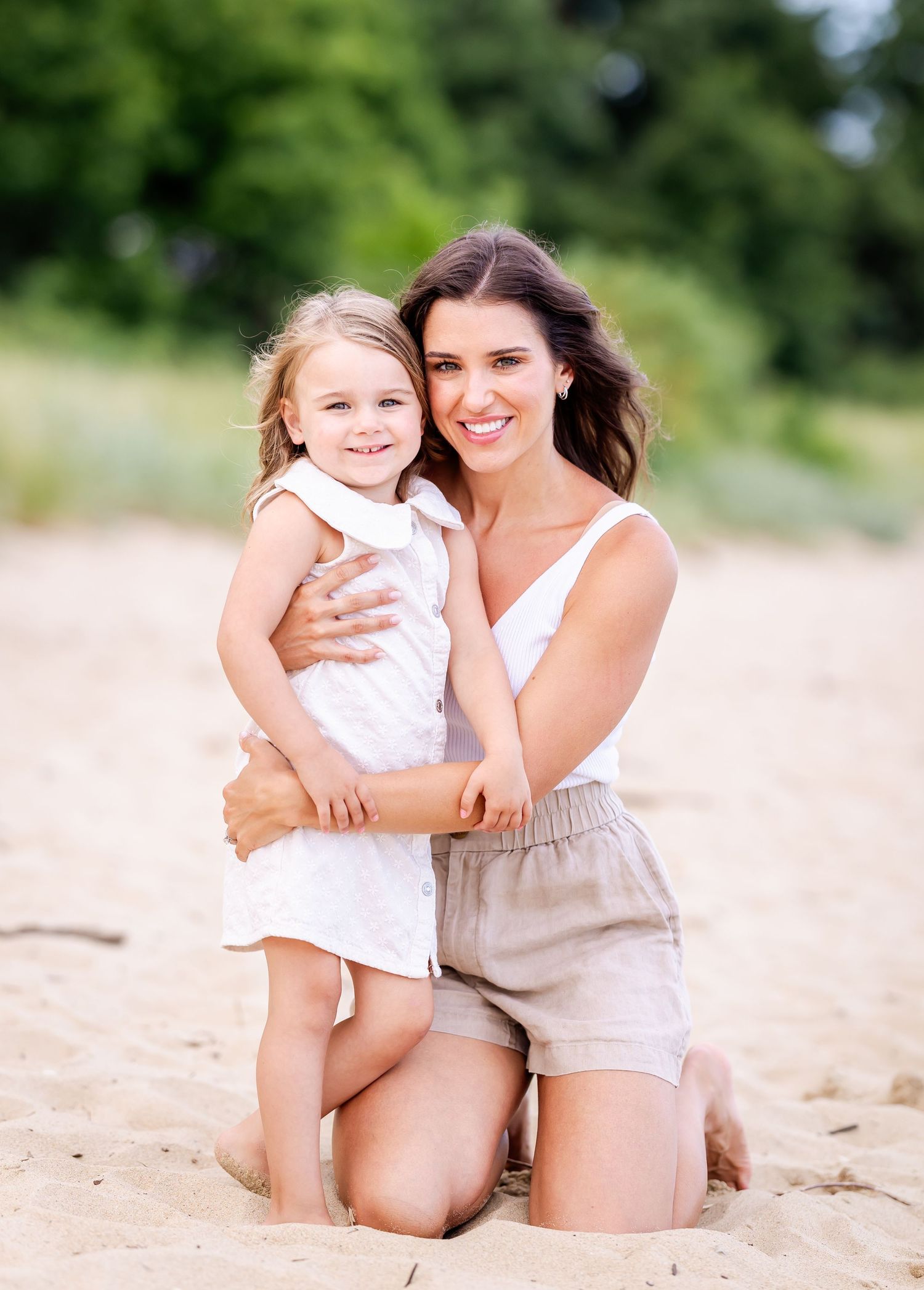 Two people sitting together on a sandy beach in casual summer attire enjoying a tender moment.