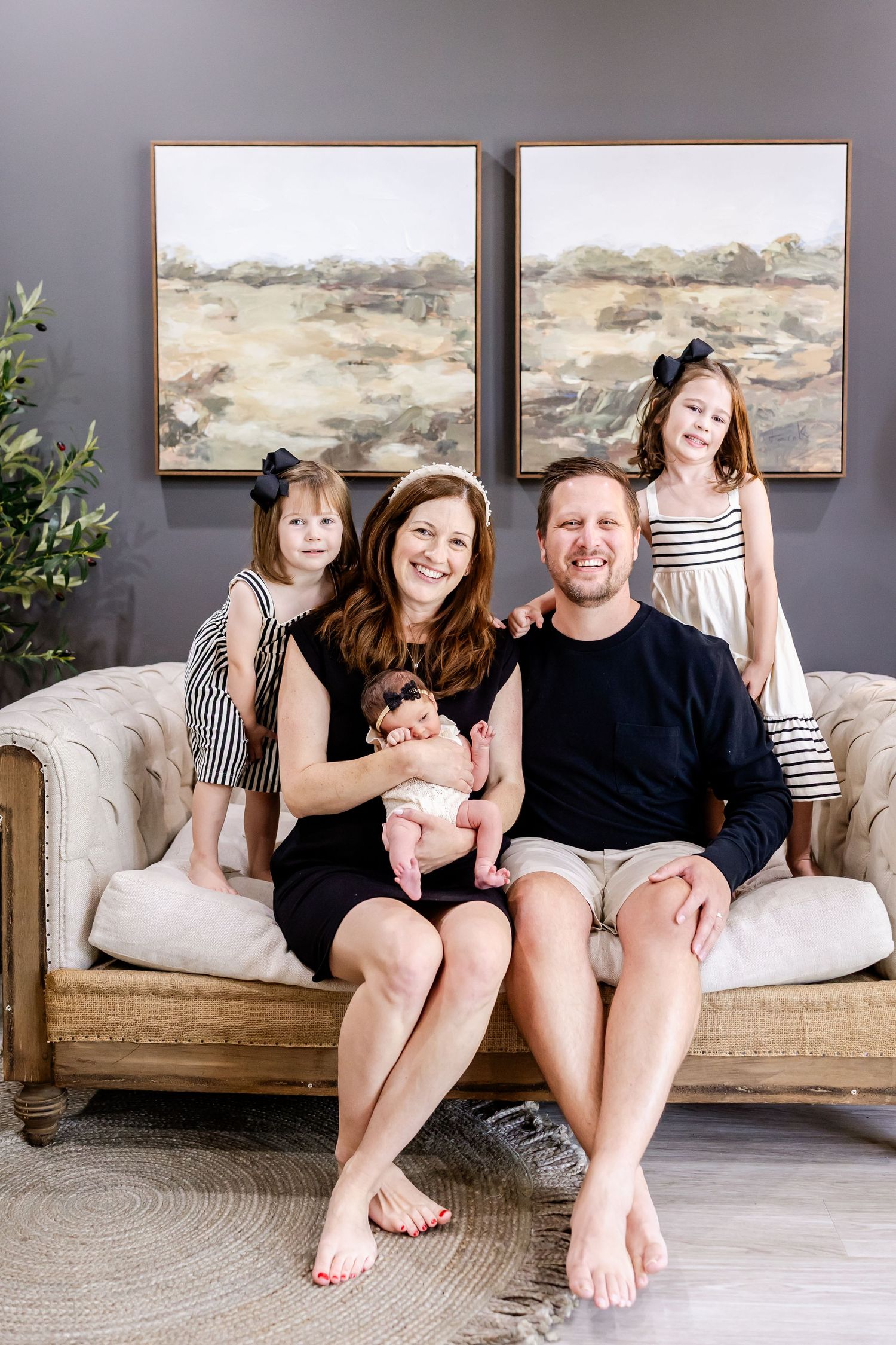 A family relaxes together on a gray couch in a modern living room with landscape artwork on the wall.