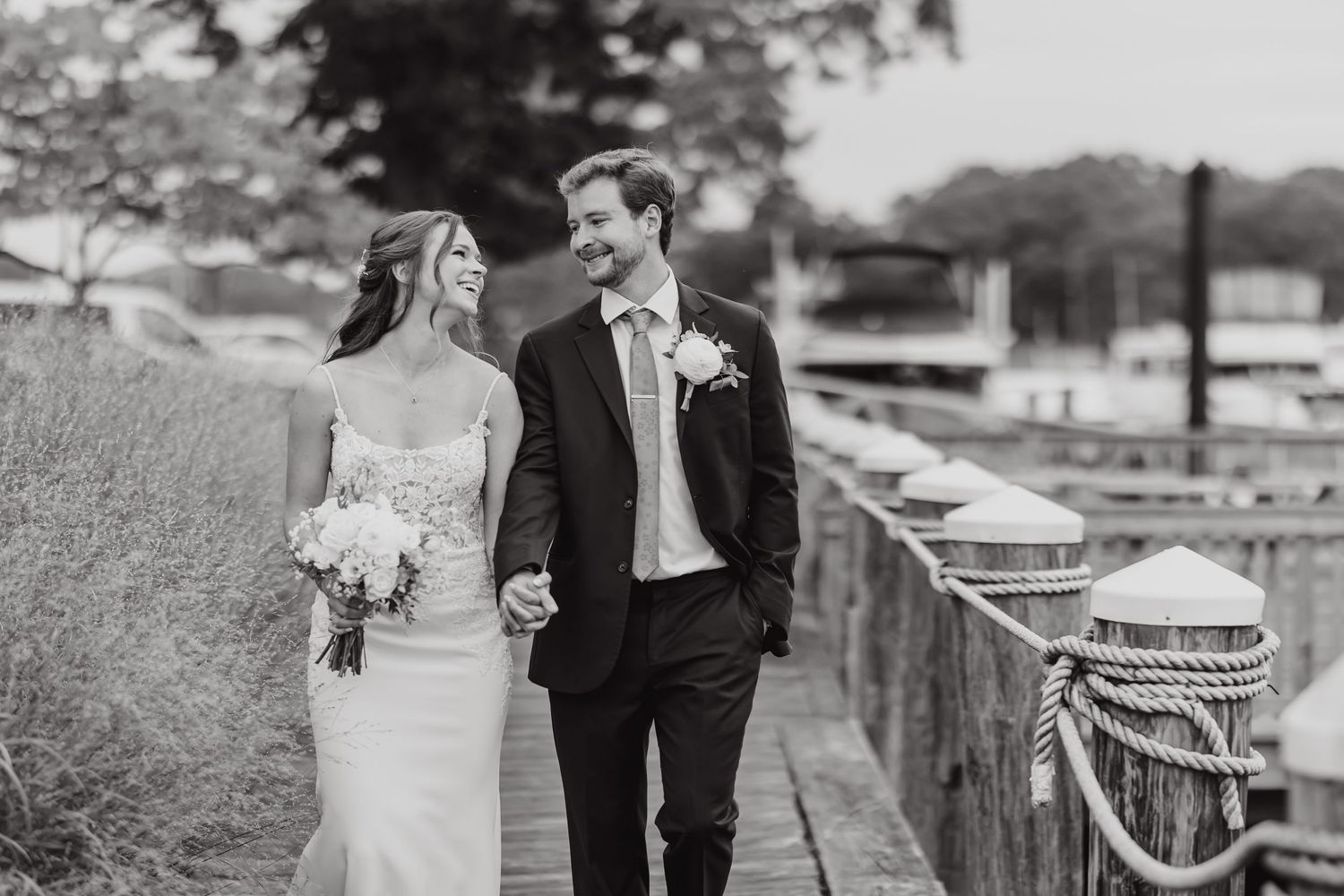 Black and white photo of a couple walking along a marina boardwalk.