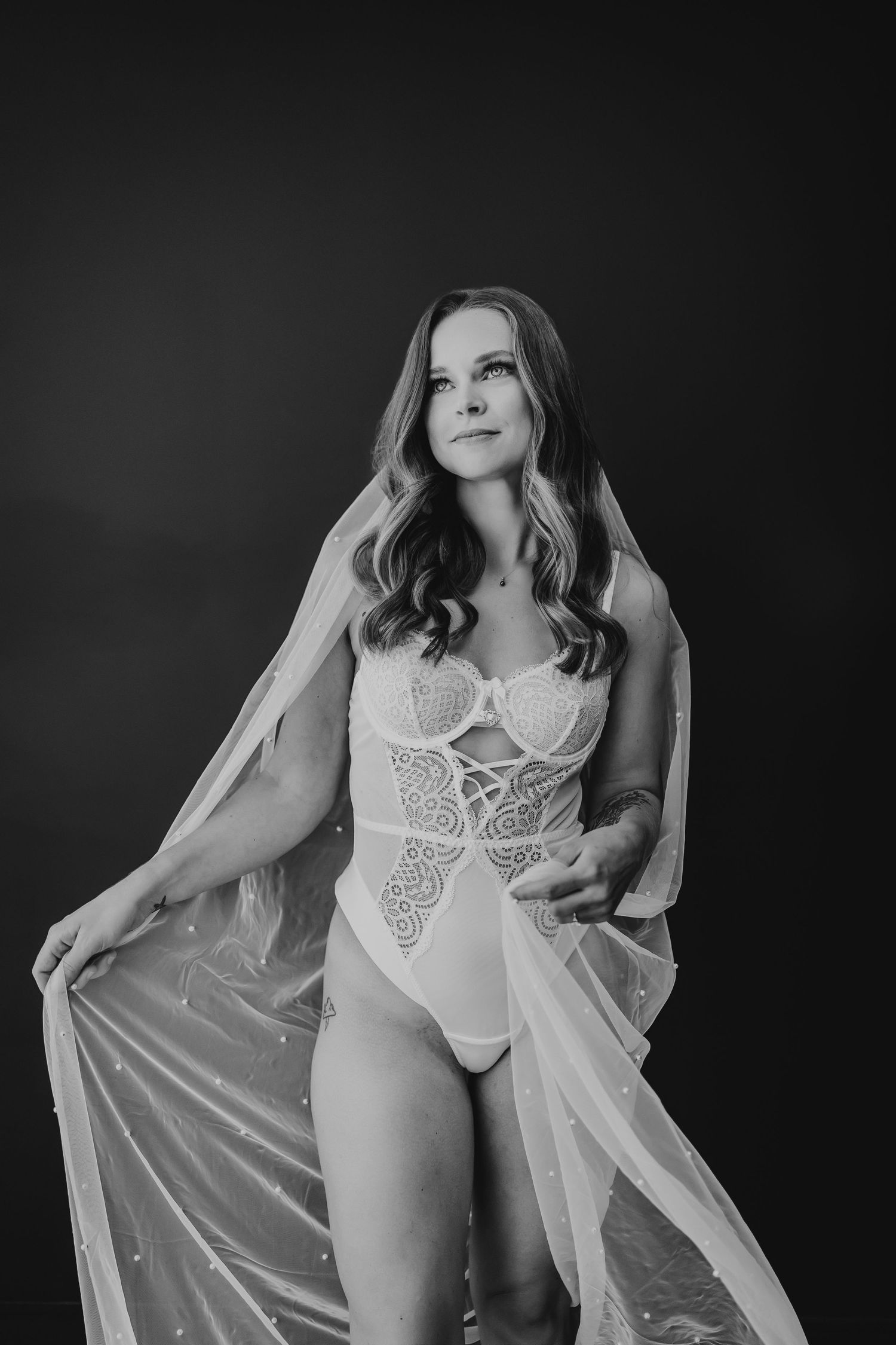 Black and white boudoir photography featuring elegant white lace lingerie and flowing sheer fabric.