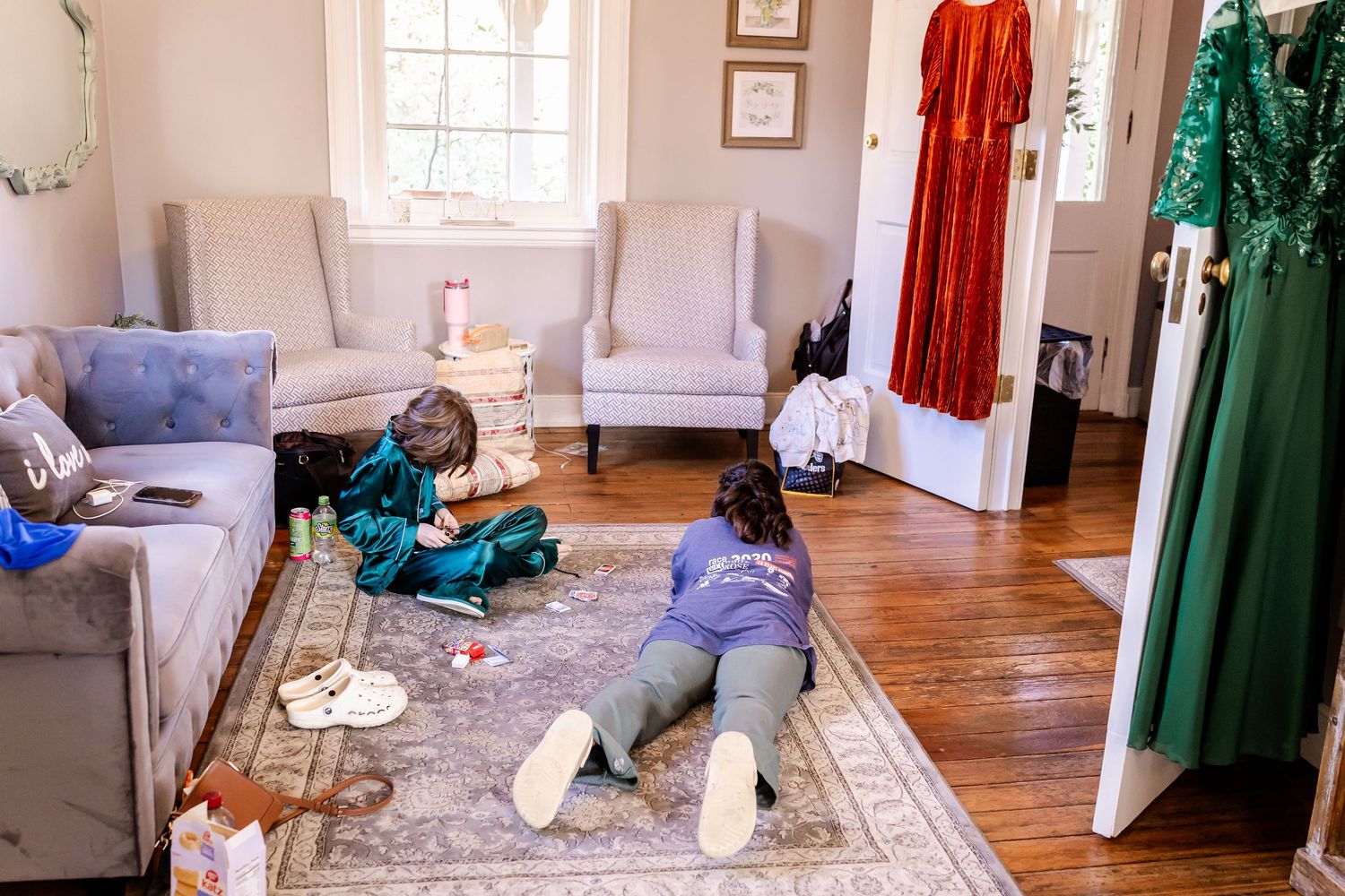 Wedding dresses in red and green hang elegantly on display in a bright sunlit room with hardwood floors.