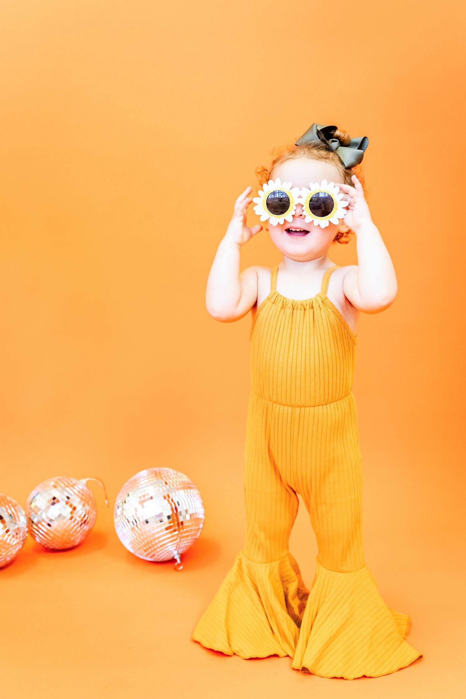 Baby in yellow overalls playing with Easter eggs on bright orange background.