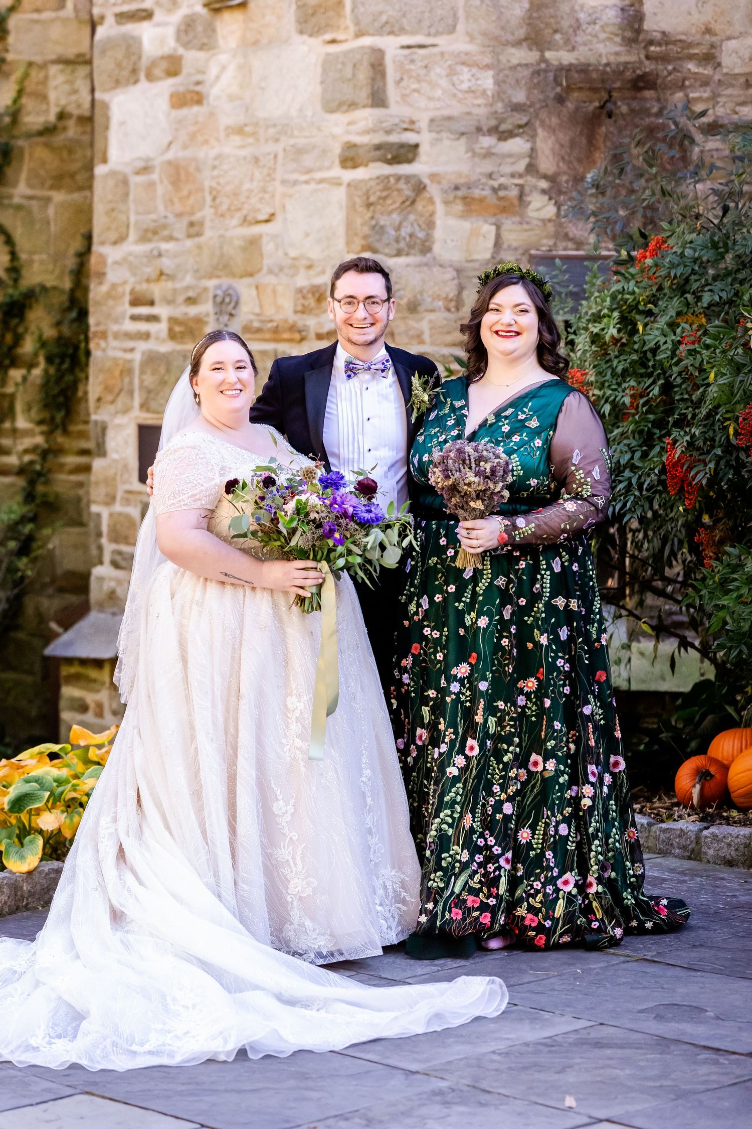 Wedding party poses with autumn decorations against a stone church wall.