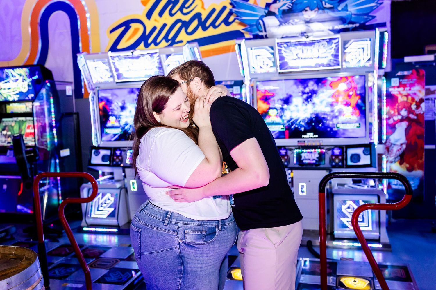 Couple sharing a romantic moment in front of vintage arcade games with neon blue signage.