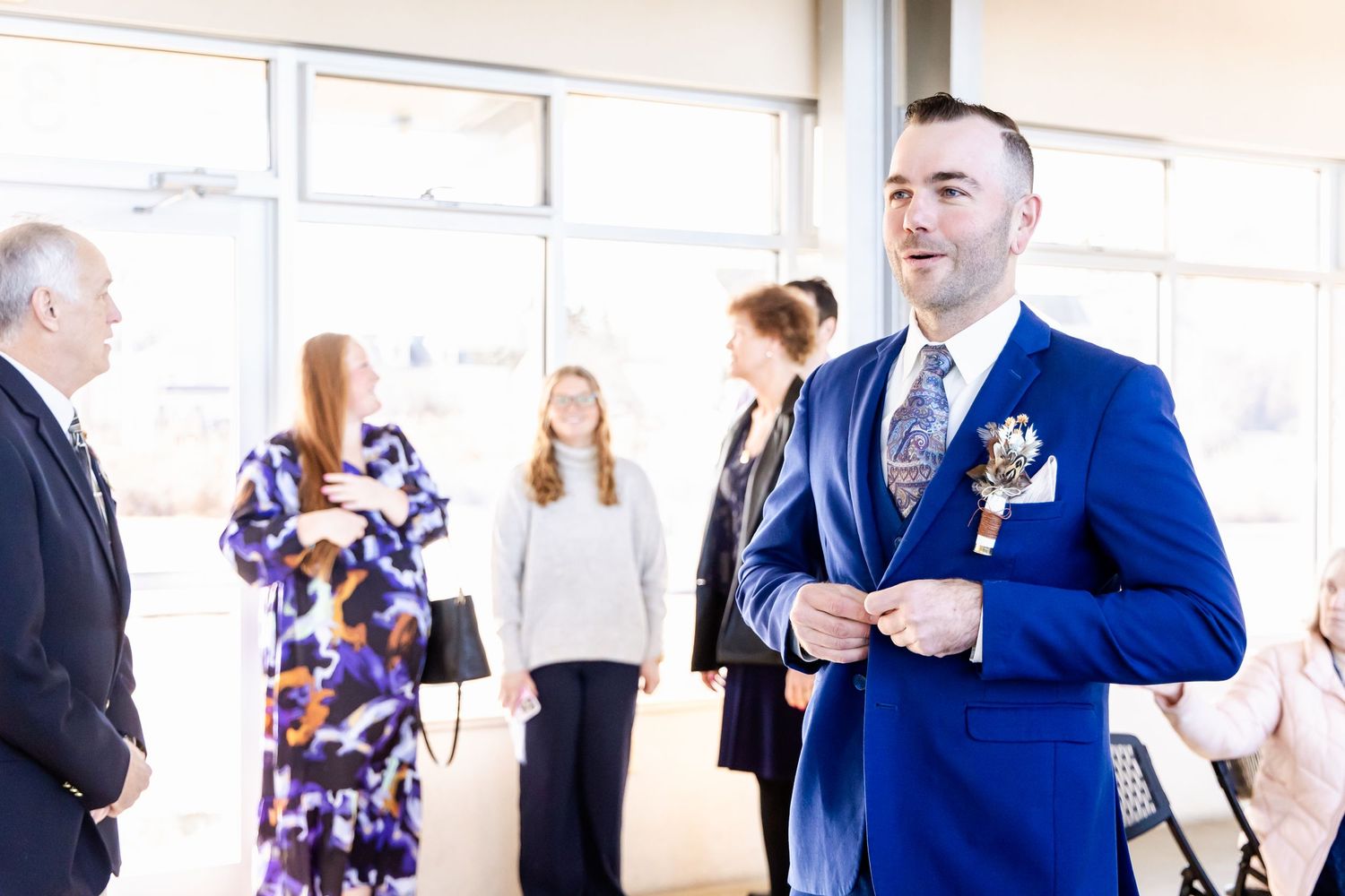 Wedding guest in bright blue suit mingles with others at reception venue.