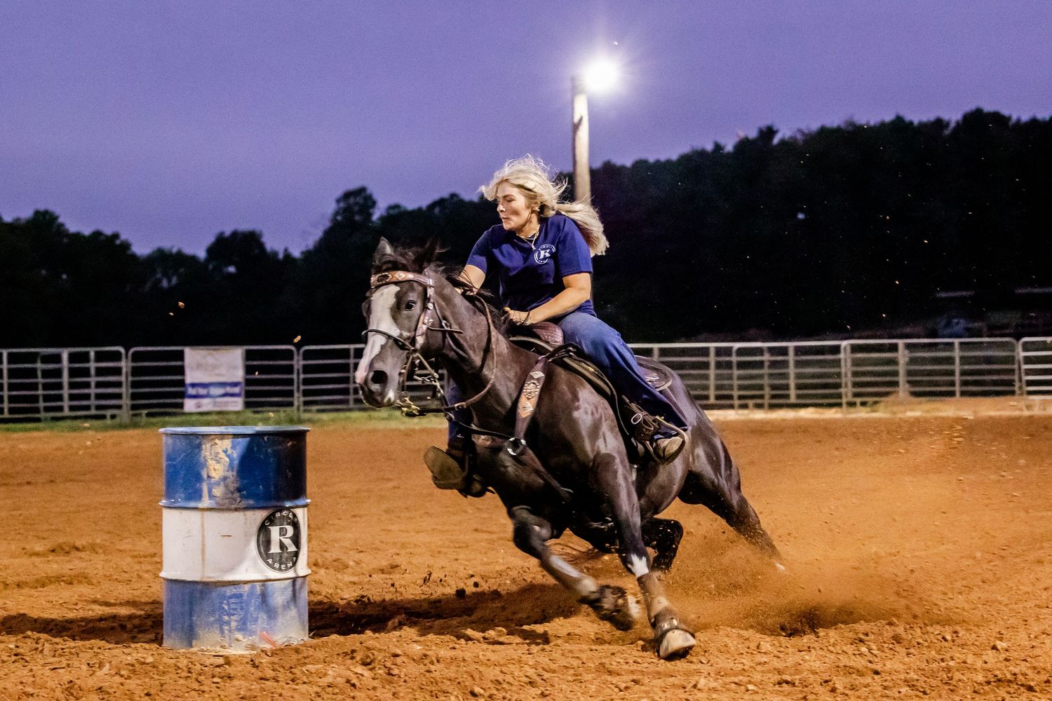 Rider and horse racing around a barrel in dramatic nighttime arena lighting.