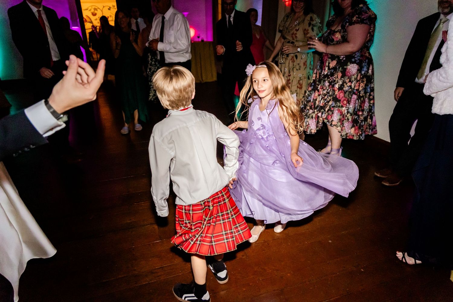 Children dancing at wedding reception with colorful lighting.