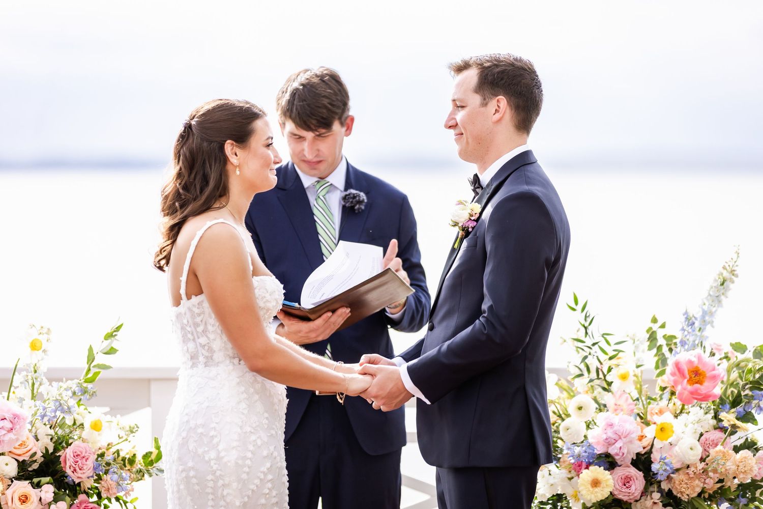 Waterfront wedding ceremony with pink and white floral arrangements.