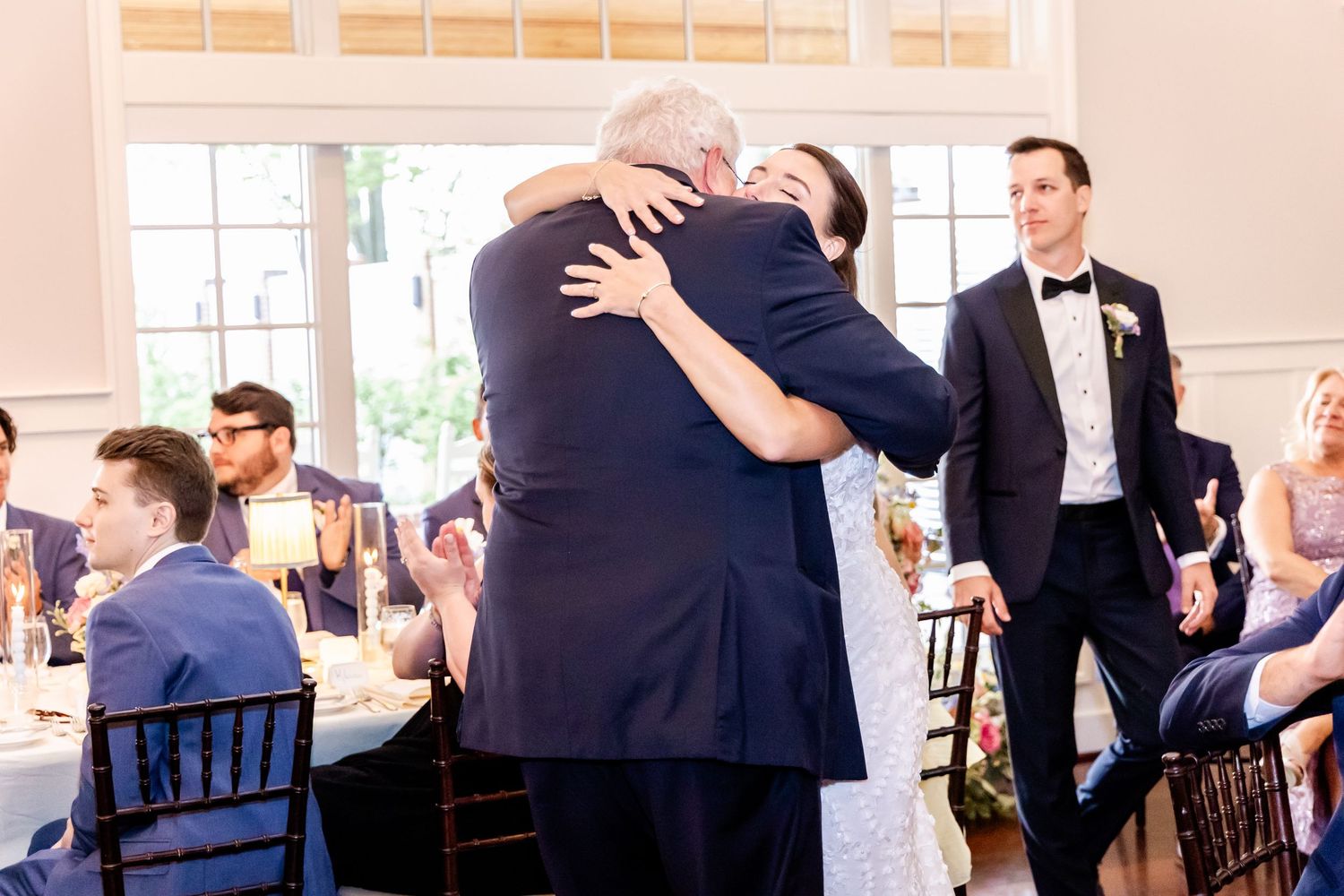 Emotional embrace shared during a wedding reception with guests seated at tables.