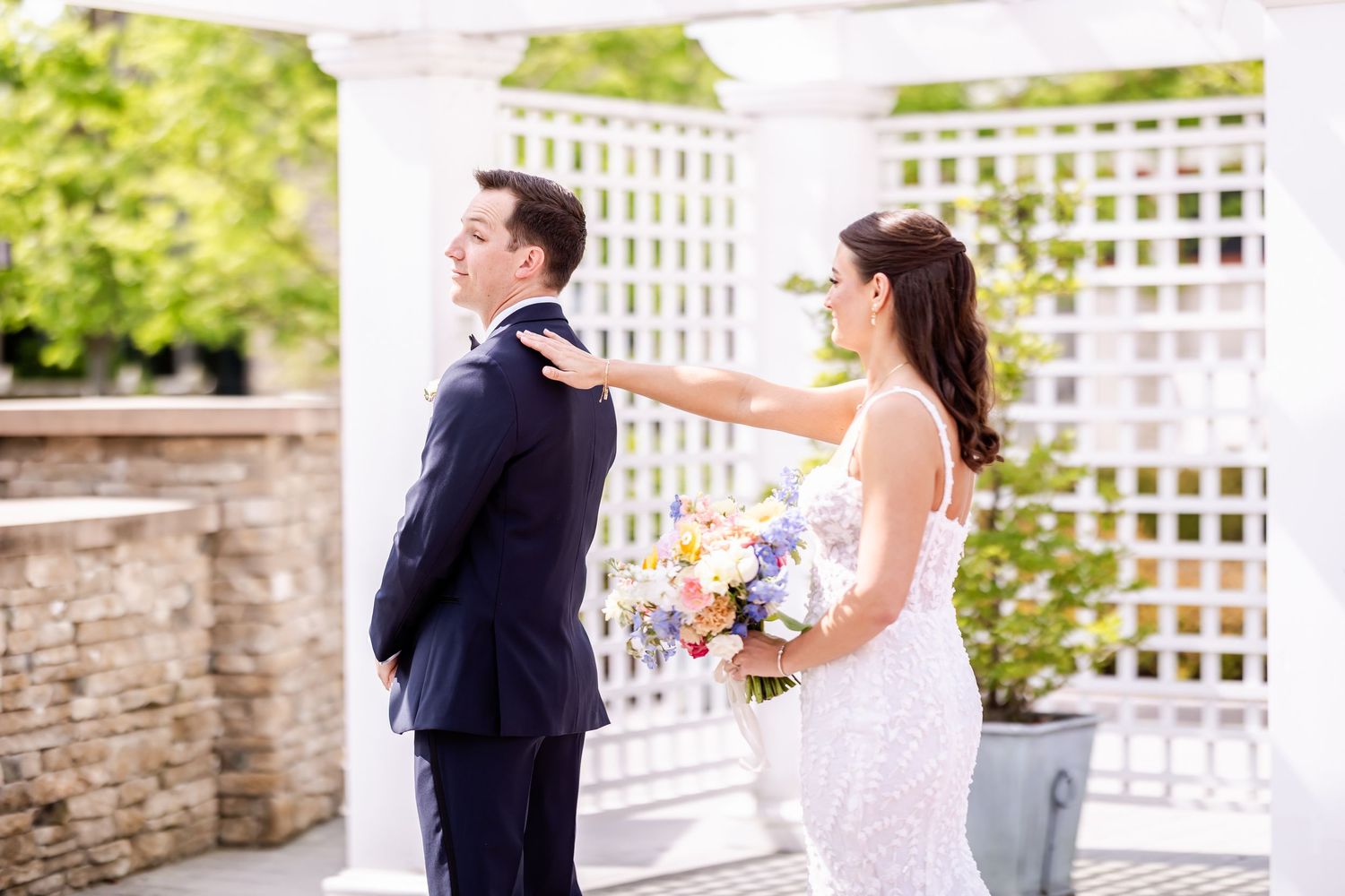 A couple shares a romantic moment on a sunny terrace with white lattice fencing and stone walls.