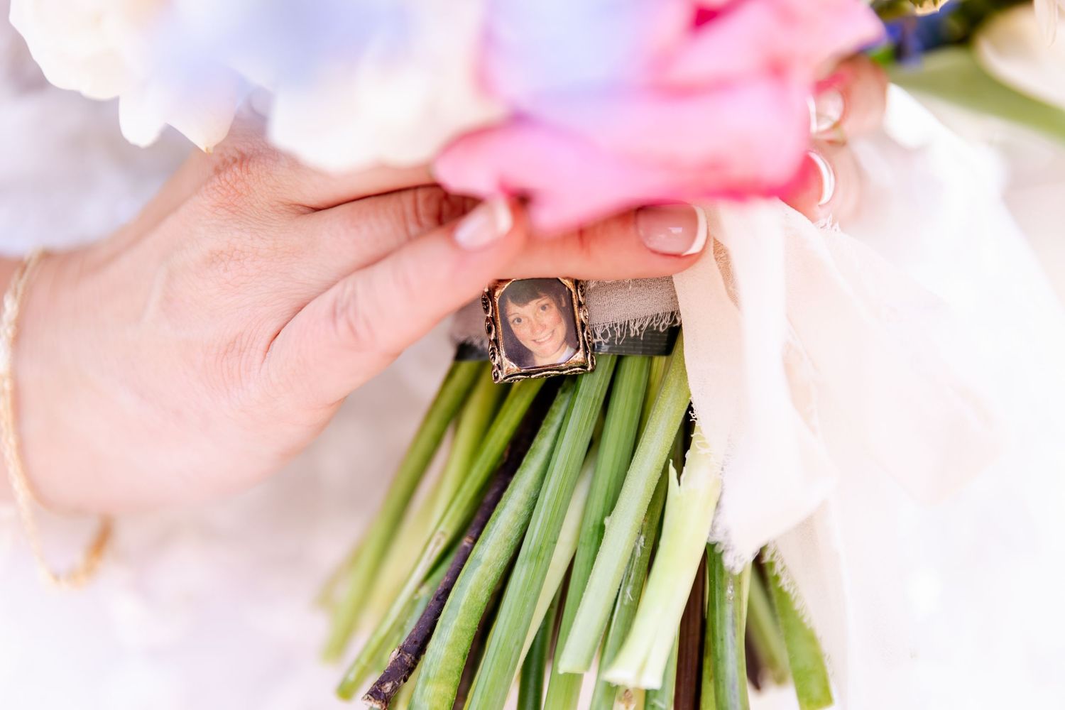 A close-up of hands holding a bridal bouquet with a small photo charm attached to the stems.