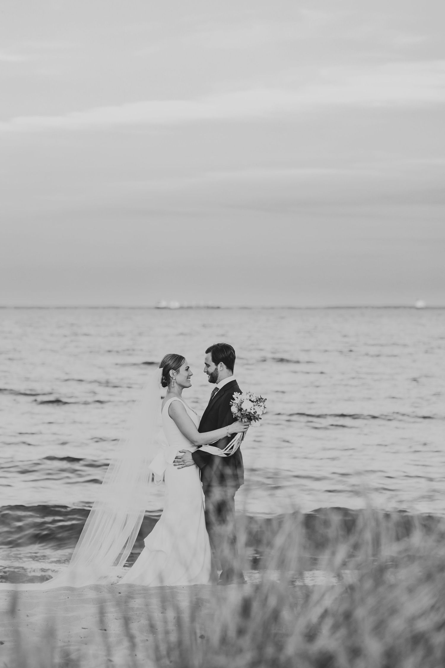 A romantic black and white portrait of a bride and groom sharing an intimate moment by the ocean.