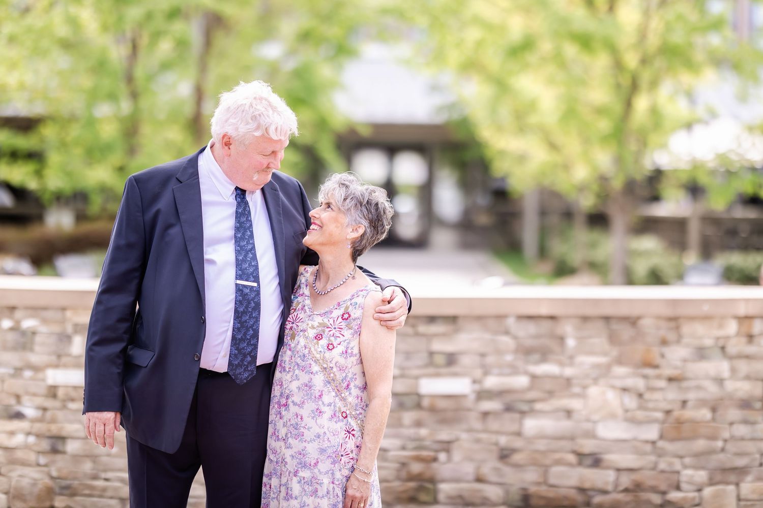 A couple shares a joyful moment together on a stone wall patio during a sunny afternoon.