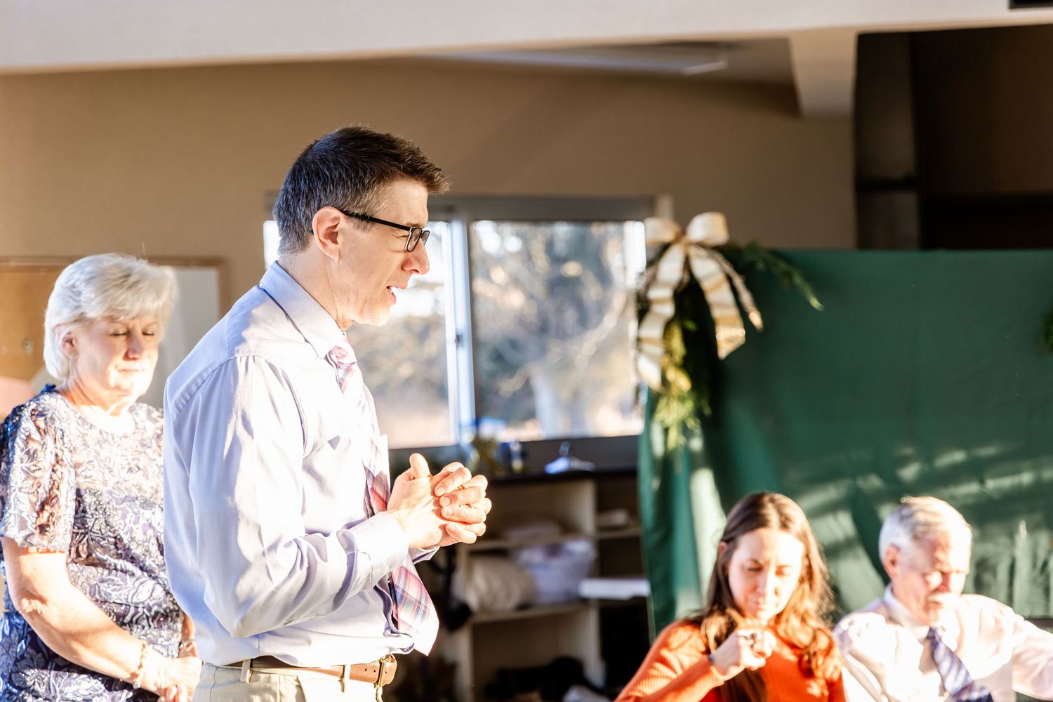 People gathered indoors at a social event with natural lighting streaming through windows in the background.