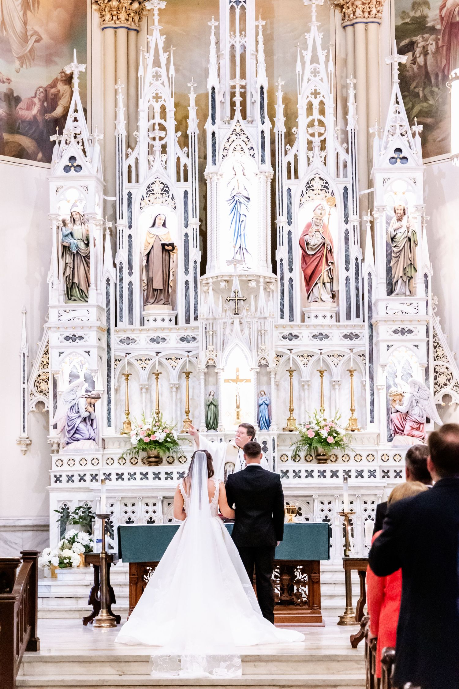 Ornate white cathedral altar with Gothic architectural details and stained glass during wedding ceremony.