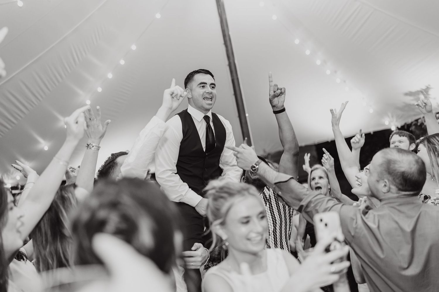 Black and white photo of wedding guests dancing and celebrating at reception.