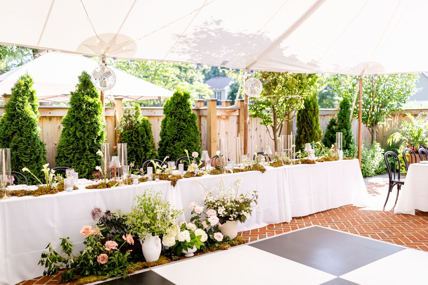 Outdoor wedding venue setup with white decor, umbrellas and floral arrangements along a pathway.