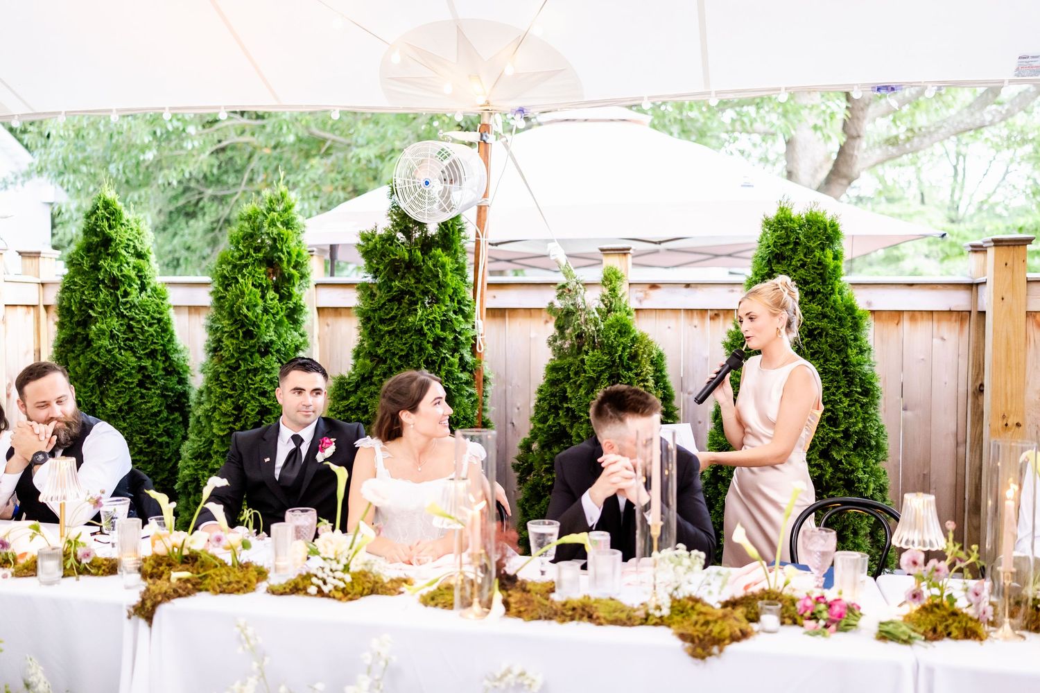 Wedding guests celebrate and dance together at an outdoor reception with string lights and greenery decor.