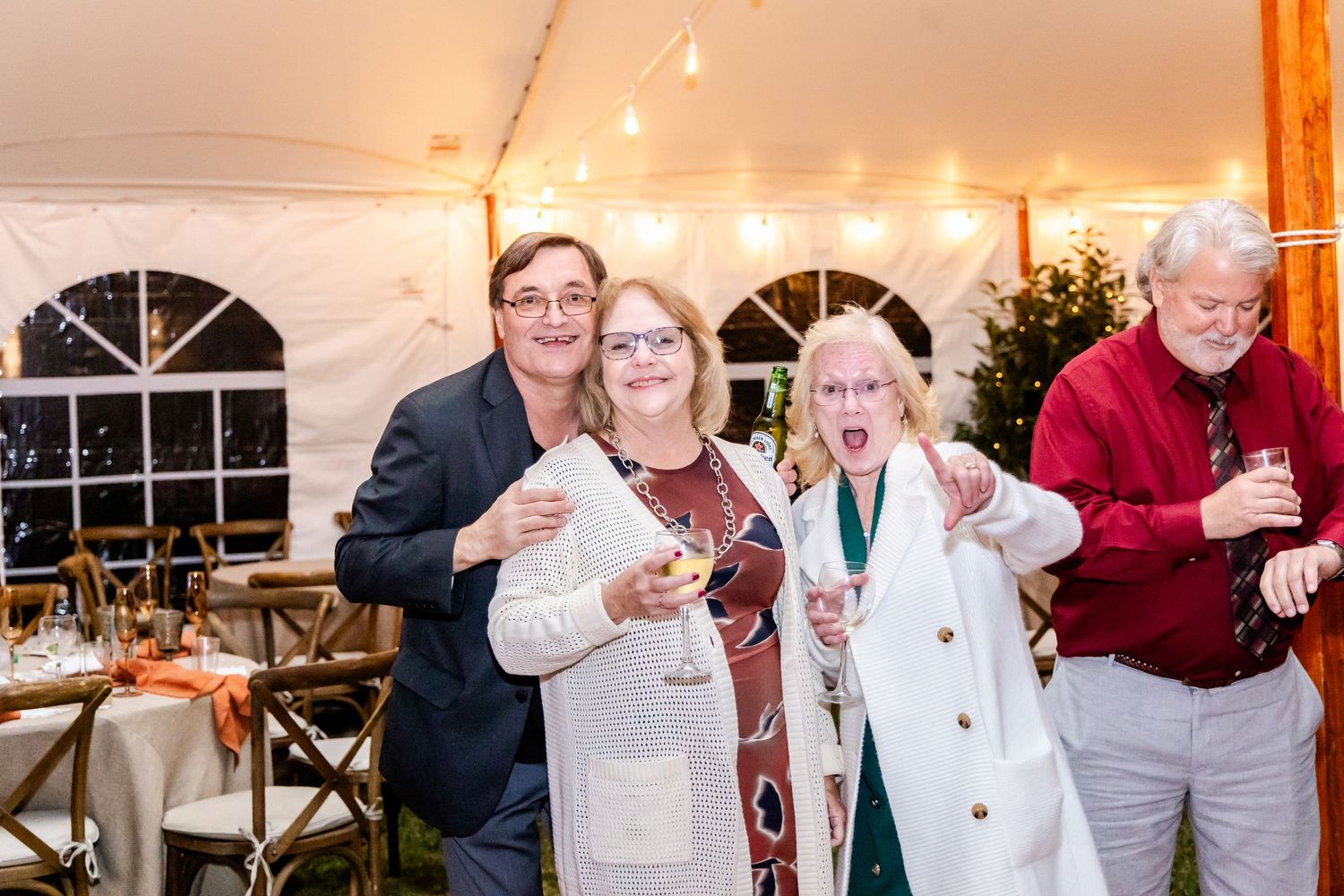 Wedding reception guests celebrating and dancing under a white tent with warm lighting.