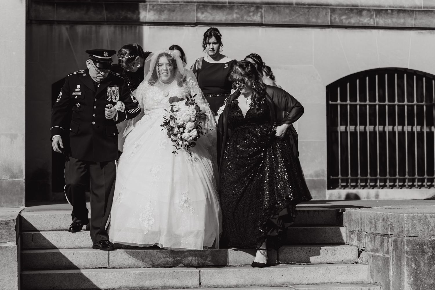 Vintage black and white photo shows wedding party posing on stone steps with bride in white gown.