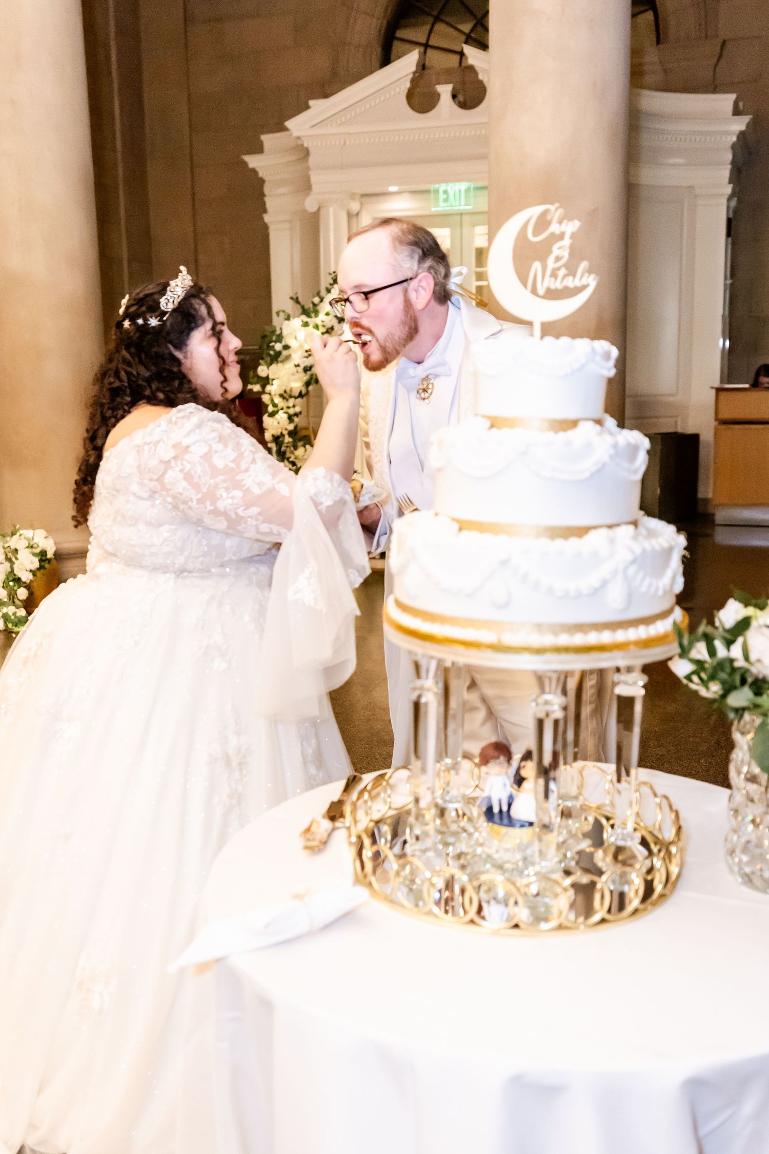 Happy couple sharing a moment while cutting their white and gold wedding cake.