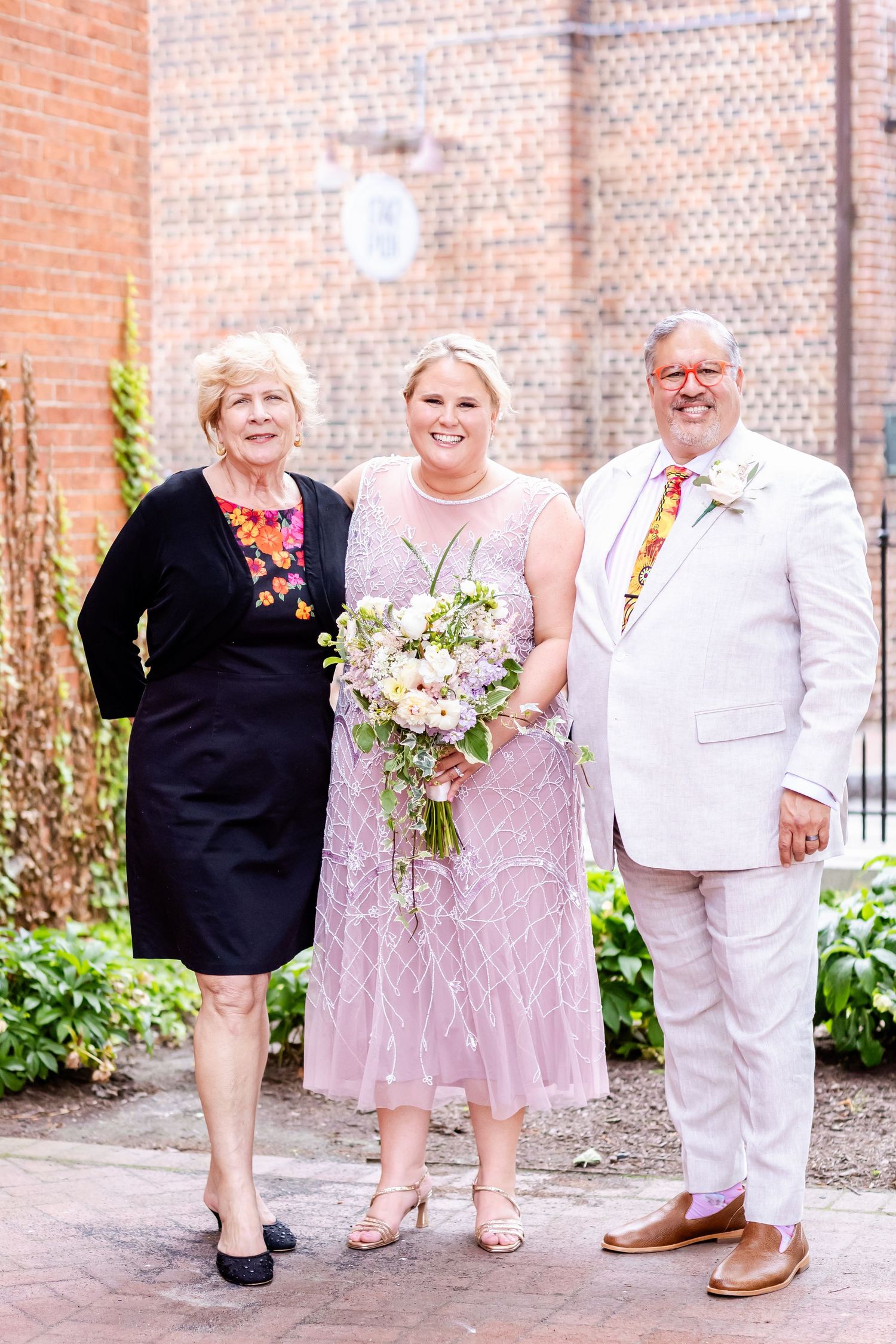 Wedding portrait with guests in formal attire against a brick wall backdrop.