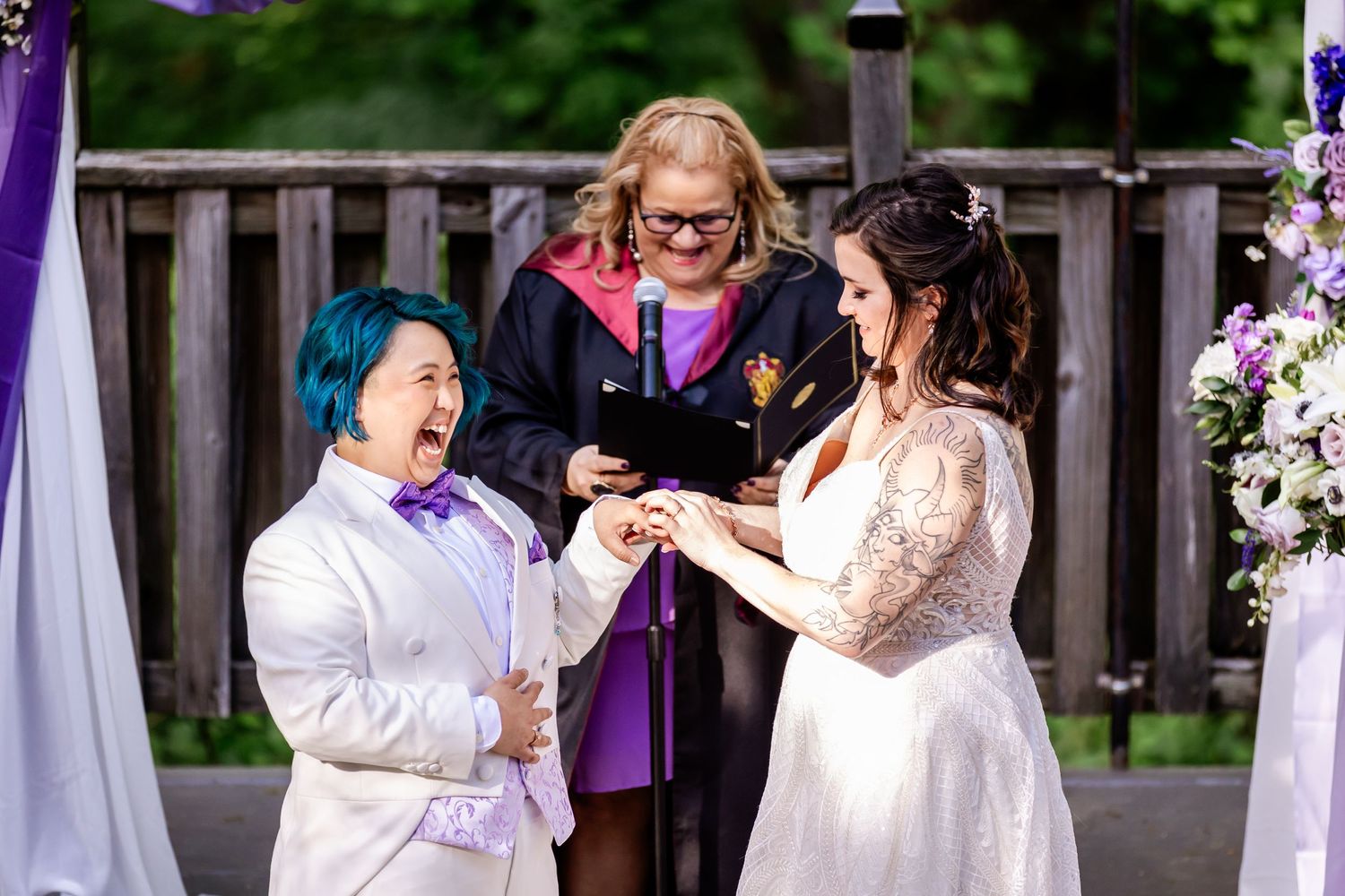 A joyful moment during a wedding ceremony as rings are exchanged under purple draped decorations.