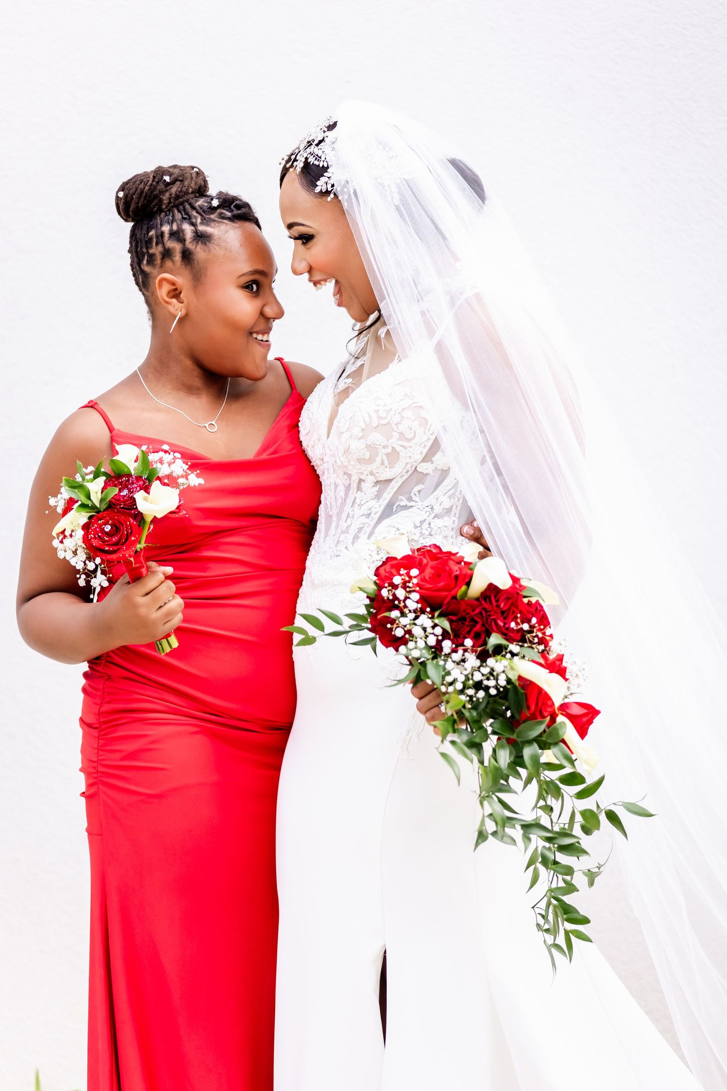 Two people share a joyful moment while holding red rose bouquets in formal attire.