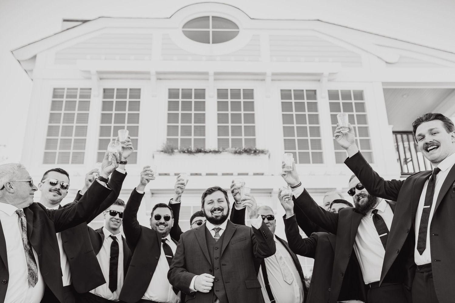 A celebratory black and white photo of groomsmen cheering outside a stately building.