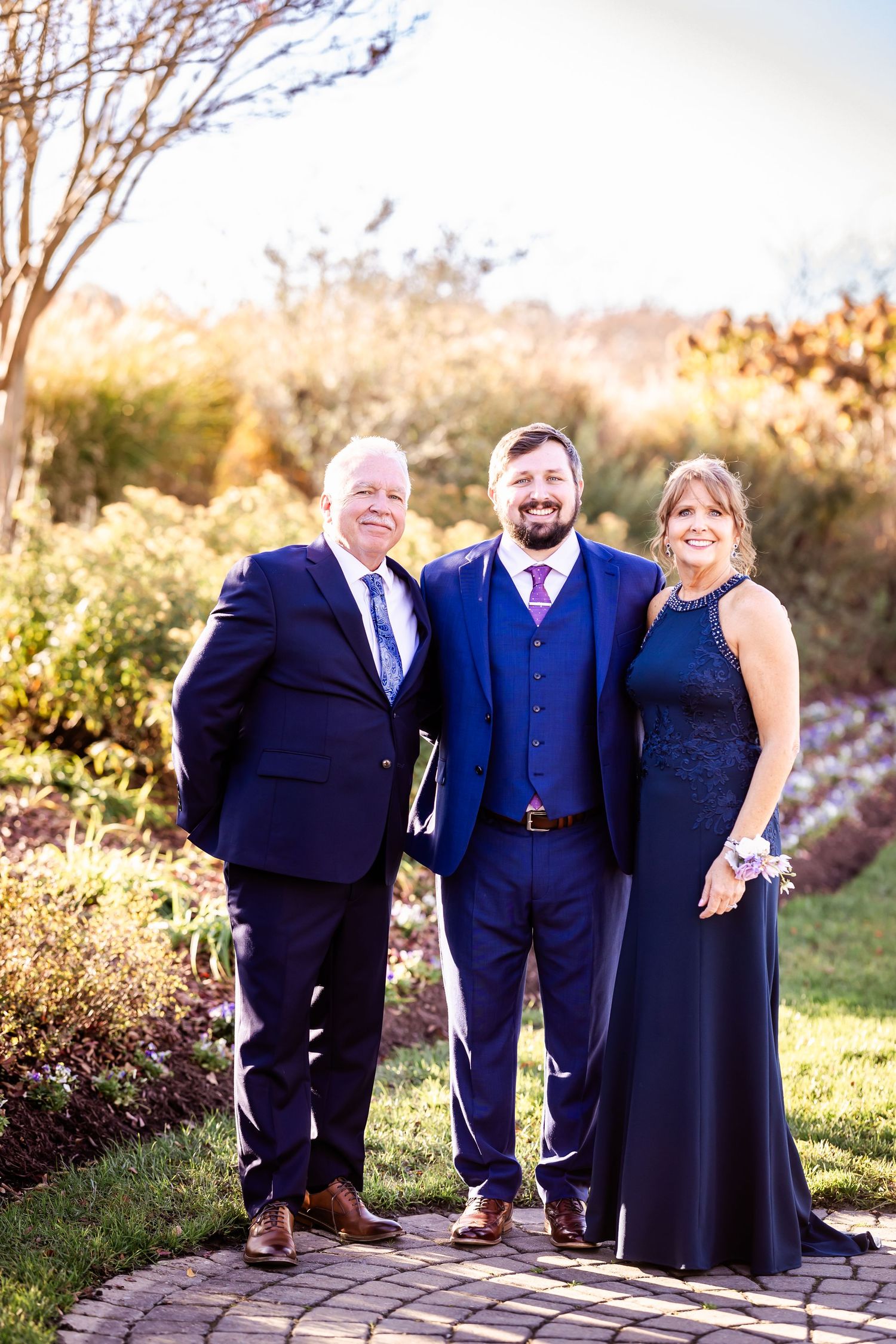 Three people in formal navy attire pose on stone path during golden hour.
