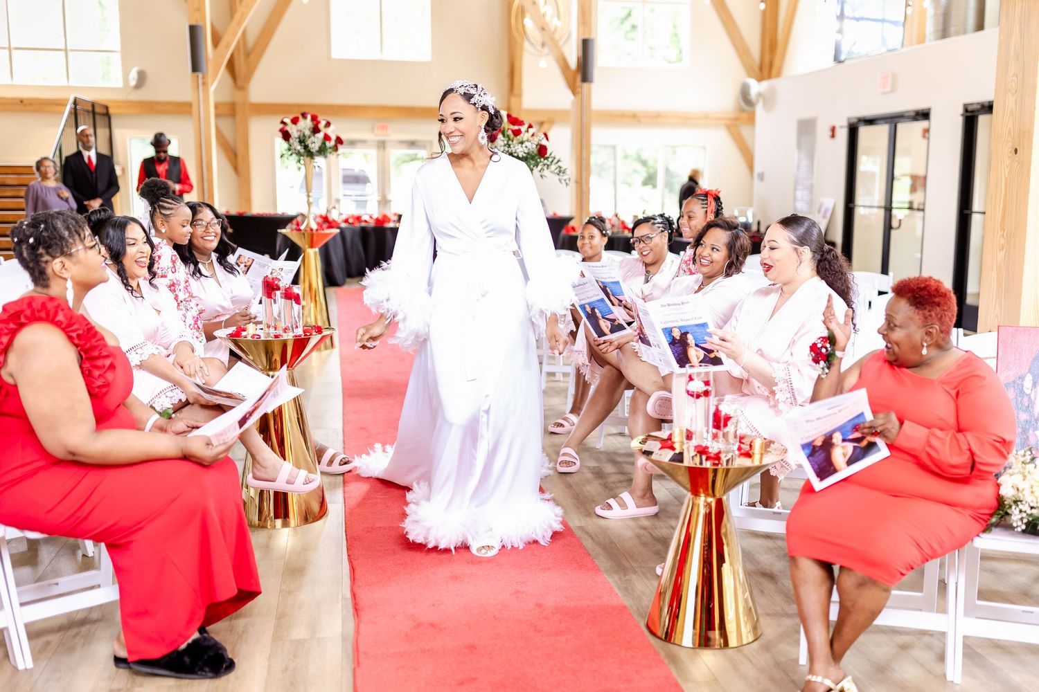 Wedding celebration in a bright venue with guests in red and white attire along a red carpet aisle.