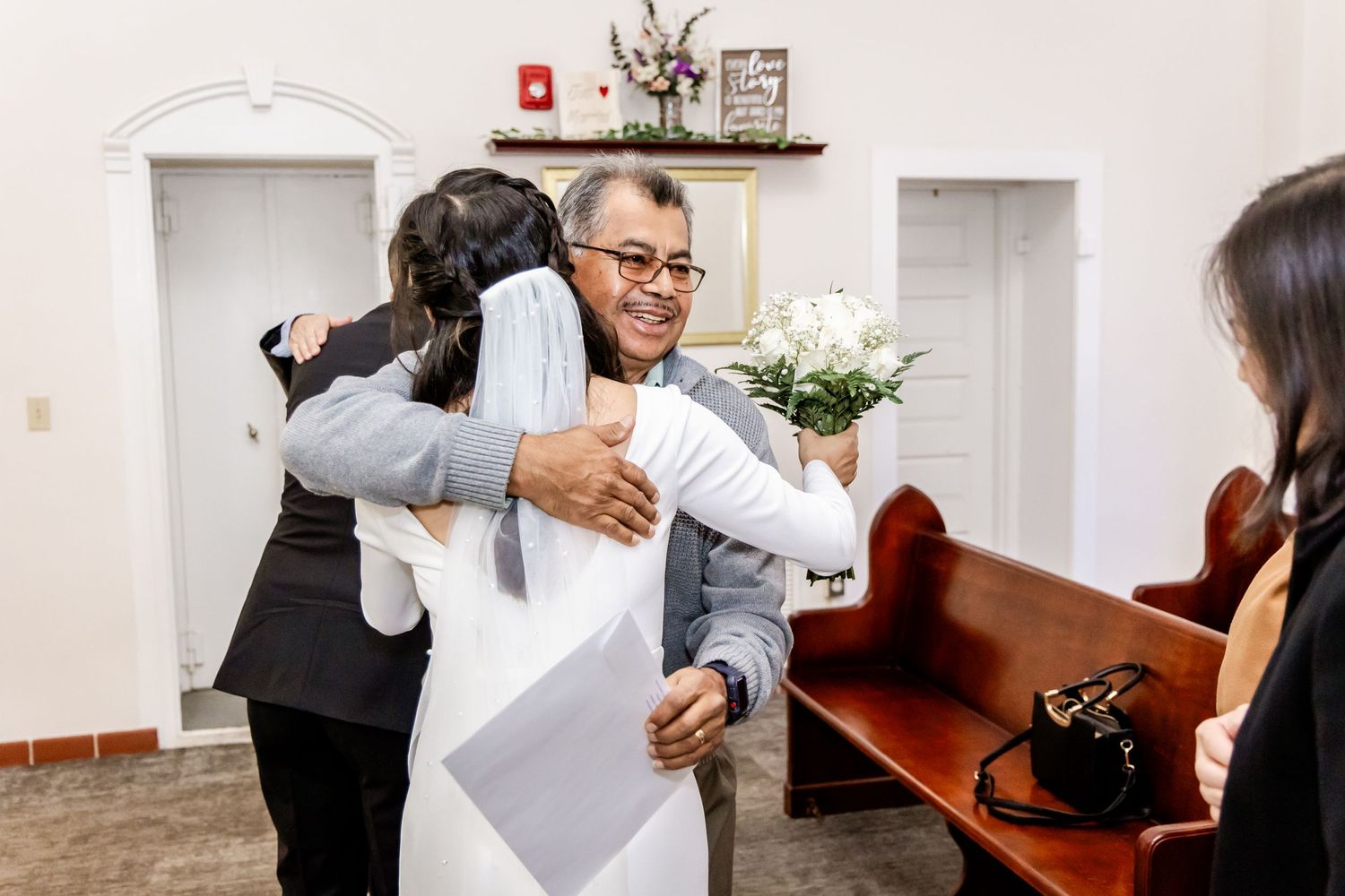 Celebratory hugs and congratulations shared after wedding ceremony in simple indoor venue.