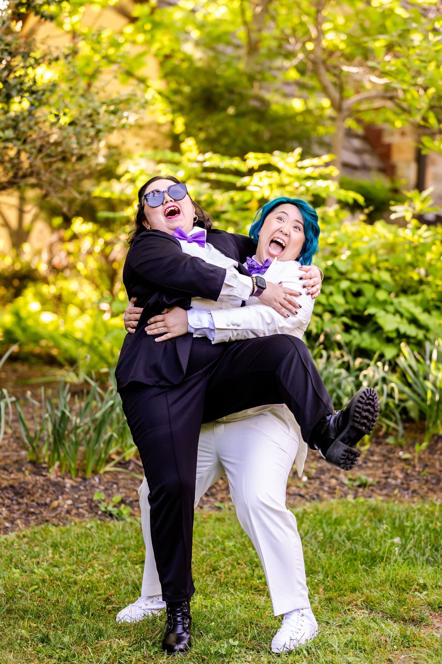 Two wedding party members sharing a fun lifting pose outdoors in contrasting black and white outfits.
